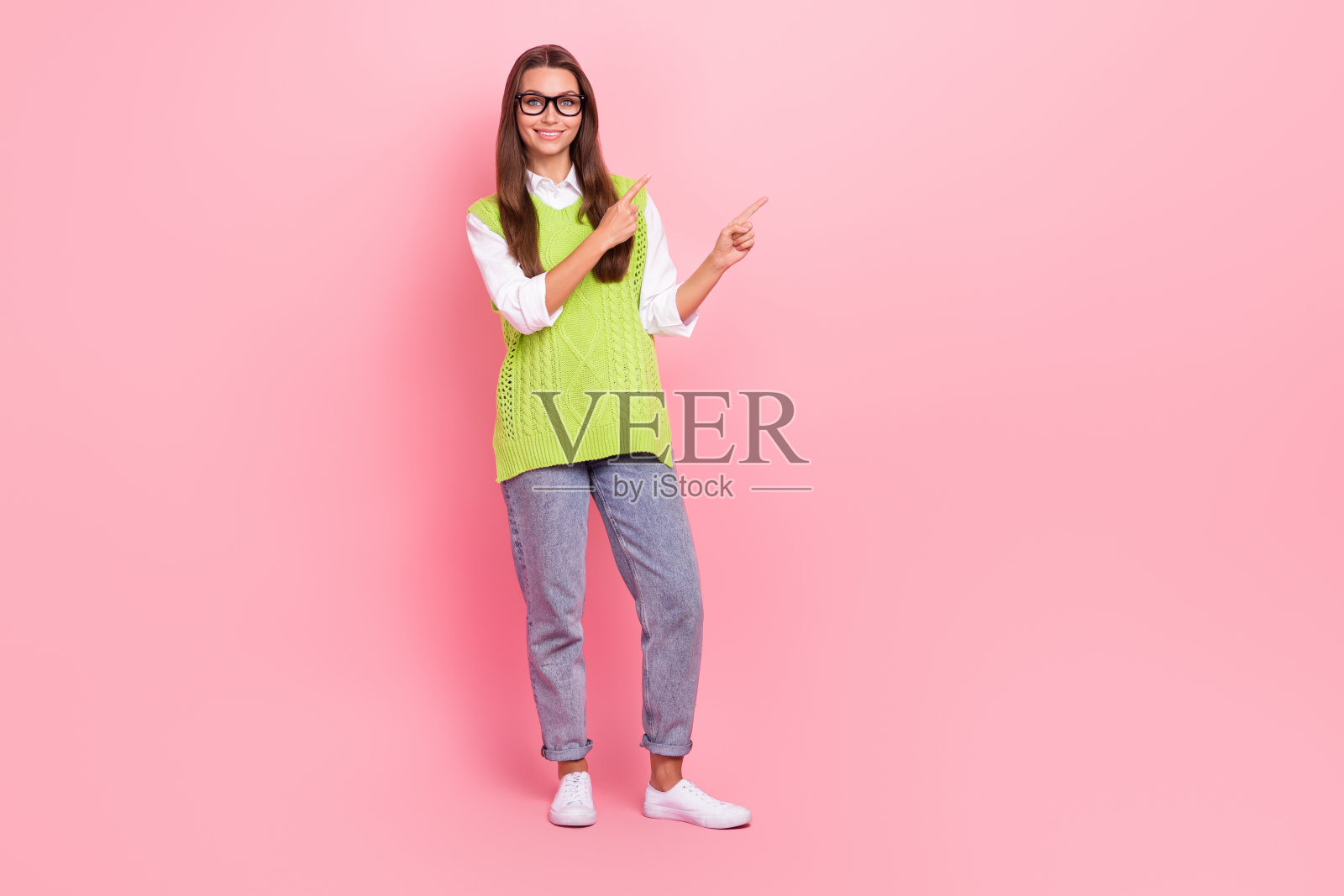 正面漂亮女孩直发的全长照片穿着绿色背心指导空白空间孤立在粉红色的背景照片摄影图片