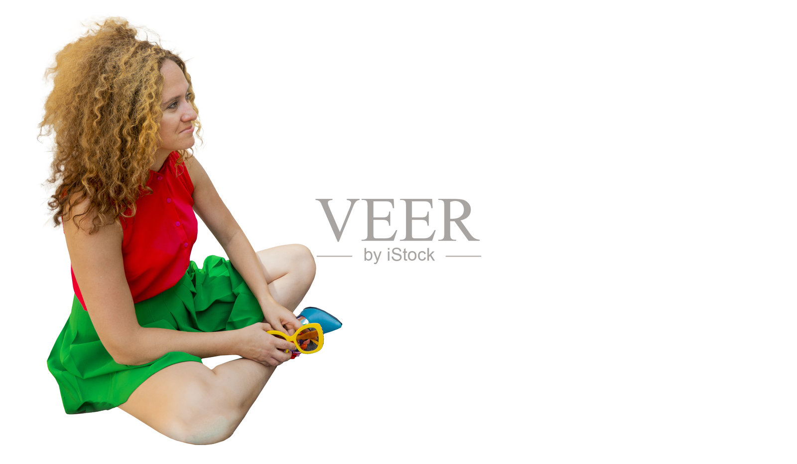 一个时髦的女人穿着鲜艳的衣服，金色的卷发，坐在莲花位在街上晒太阳和休息照片摄影图片