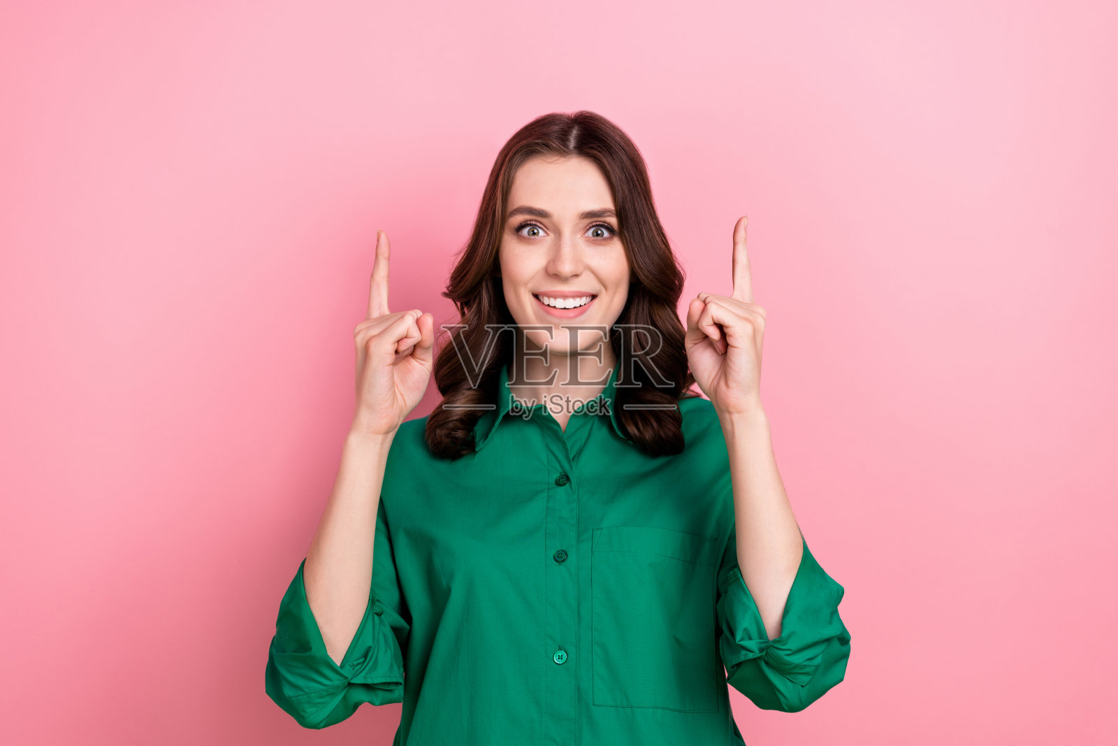 照片中穿着绿色衬衫的开朗积极的女士用两只手指指向空的空间，孤立的粉红色背景照片摄影图片