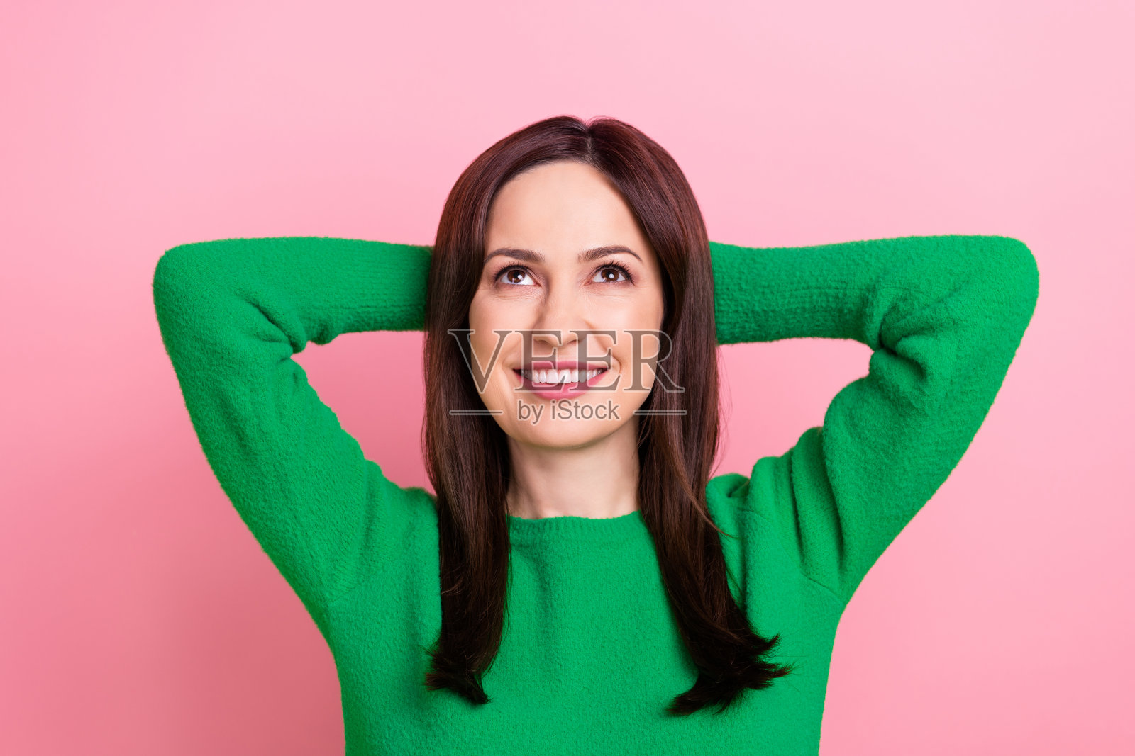 照片中开朗积极的女性戴着绿色的手臂，抬头仰望空旷的空间，孤立的粉红色背景照片摄影图片
