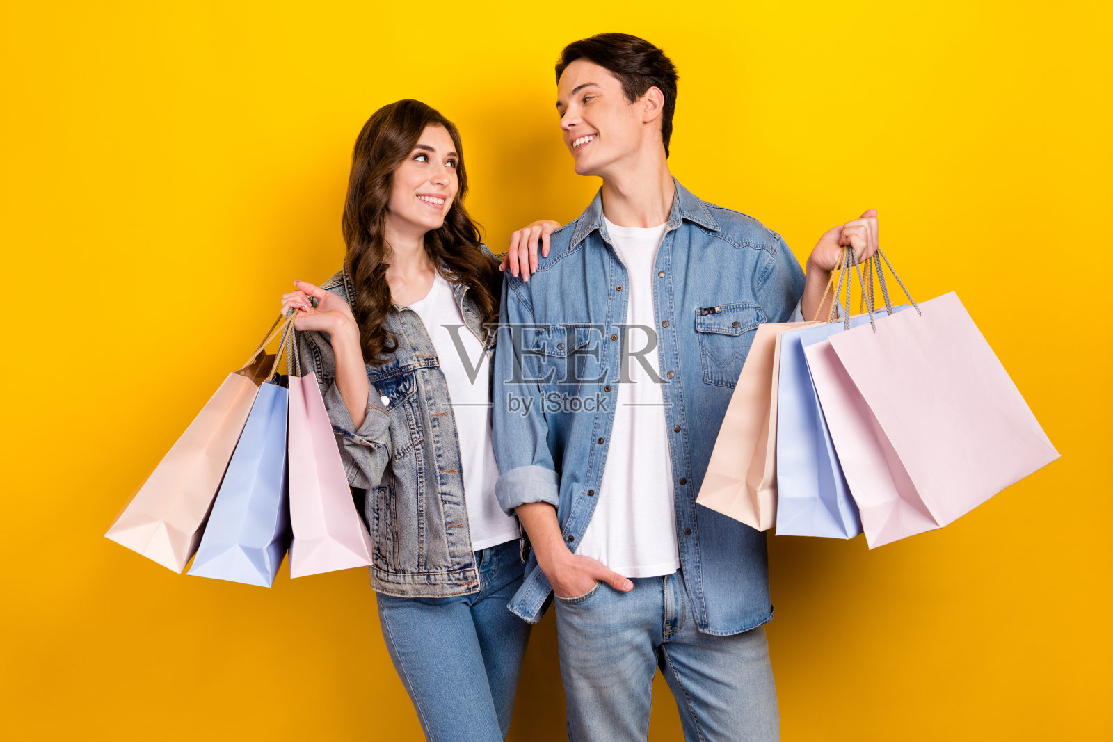 照片中，两个可爱的人相视而笑，拿着购物袋孤立在黄色背景上照片摄影图片
