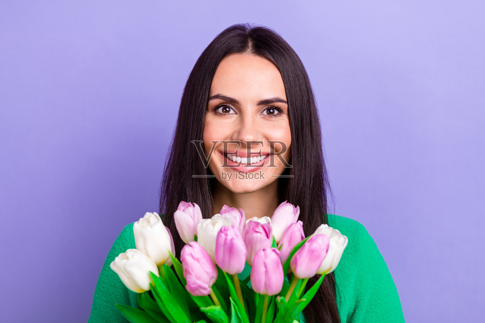 照片中闪亮可爱的女士穿着绿色毛衣微笑着拿着郁金香束孤立的紫罗兰色背景照片摄影图片