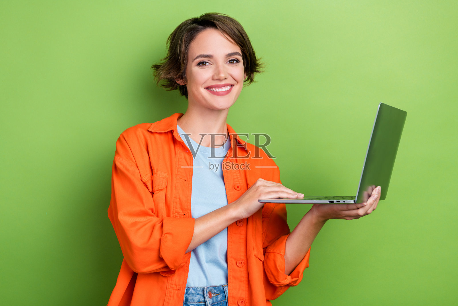 可爱的积极的女士穿着橙色时髦的衣服，拿着使用现代小工具的照片，在绿色的背景上孤立的商店照片摄影图片