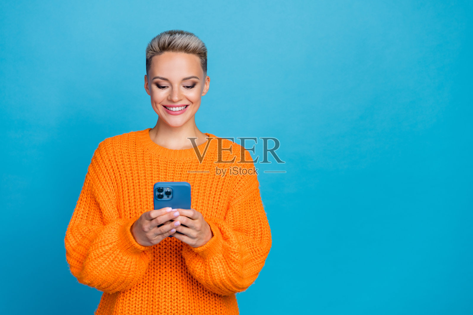照片中可爱甜美的女子穿着针织套头衫打字现代装置空白空间孤立的蓝色背景照片摄影图片
