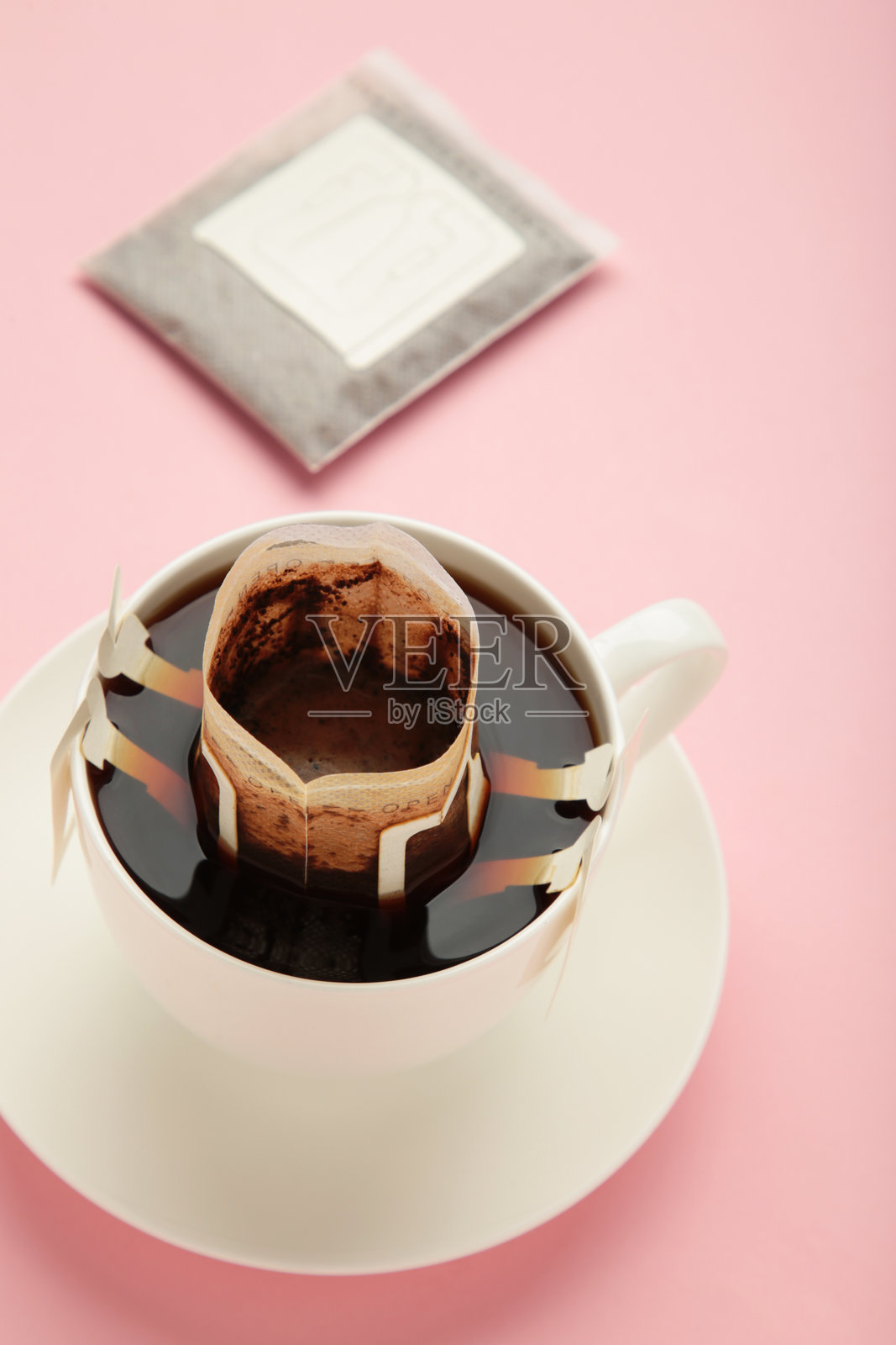 滴咖啡袋与磨碎的咖啡在杯子上粉红色的背景。垂直图照片摄影图片