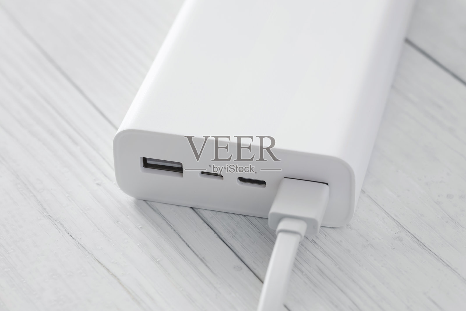 白色移动电源的特写，有多个usb接口，其中一个有插入的电缆。借助充电宝为设备充电照片摄影图片