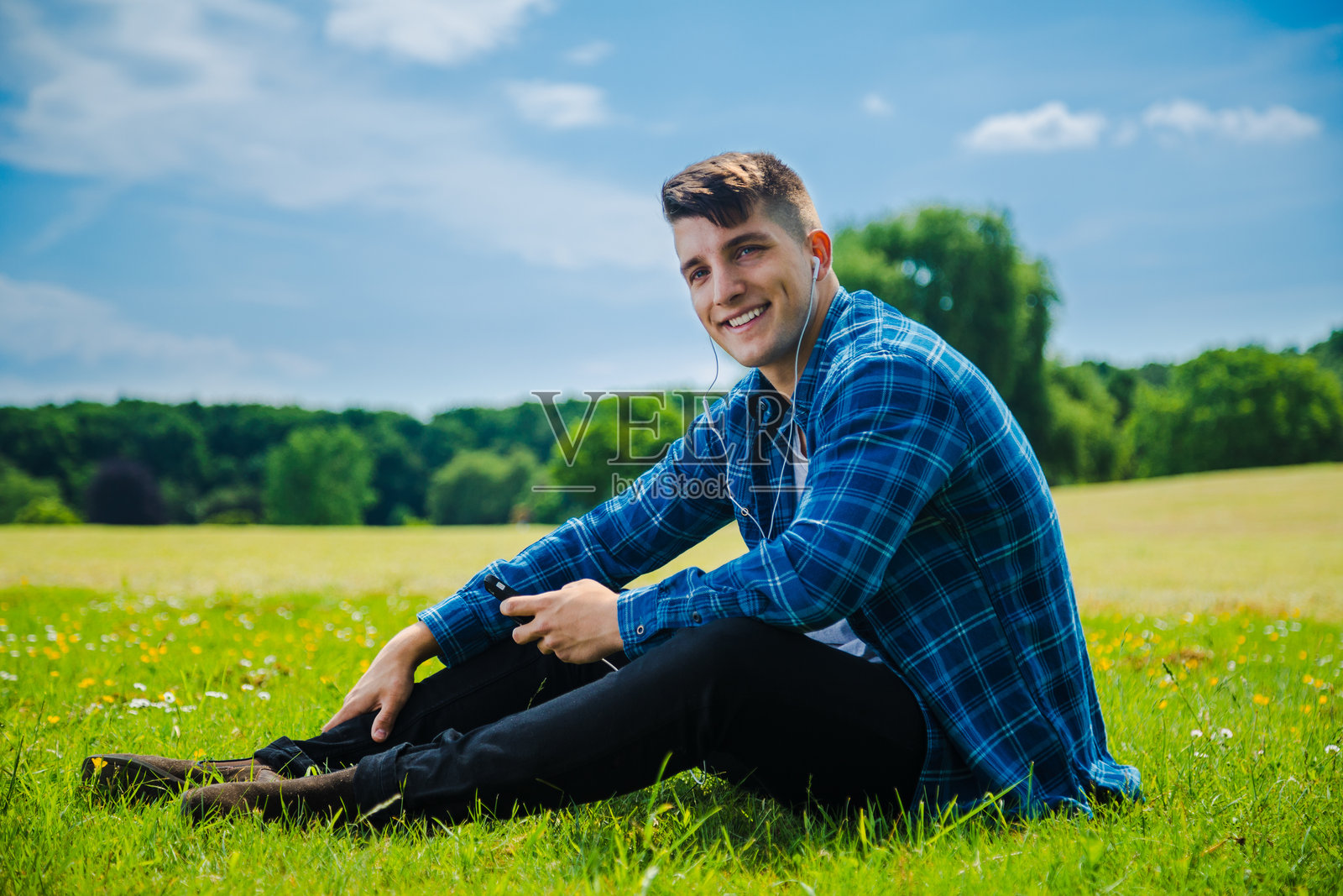 一个年轻人坐在草地上，戴着入耳式耳机听音乐照片摄影图片