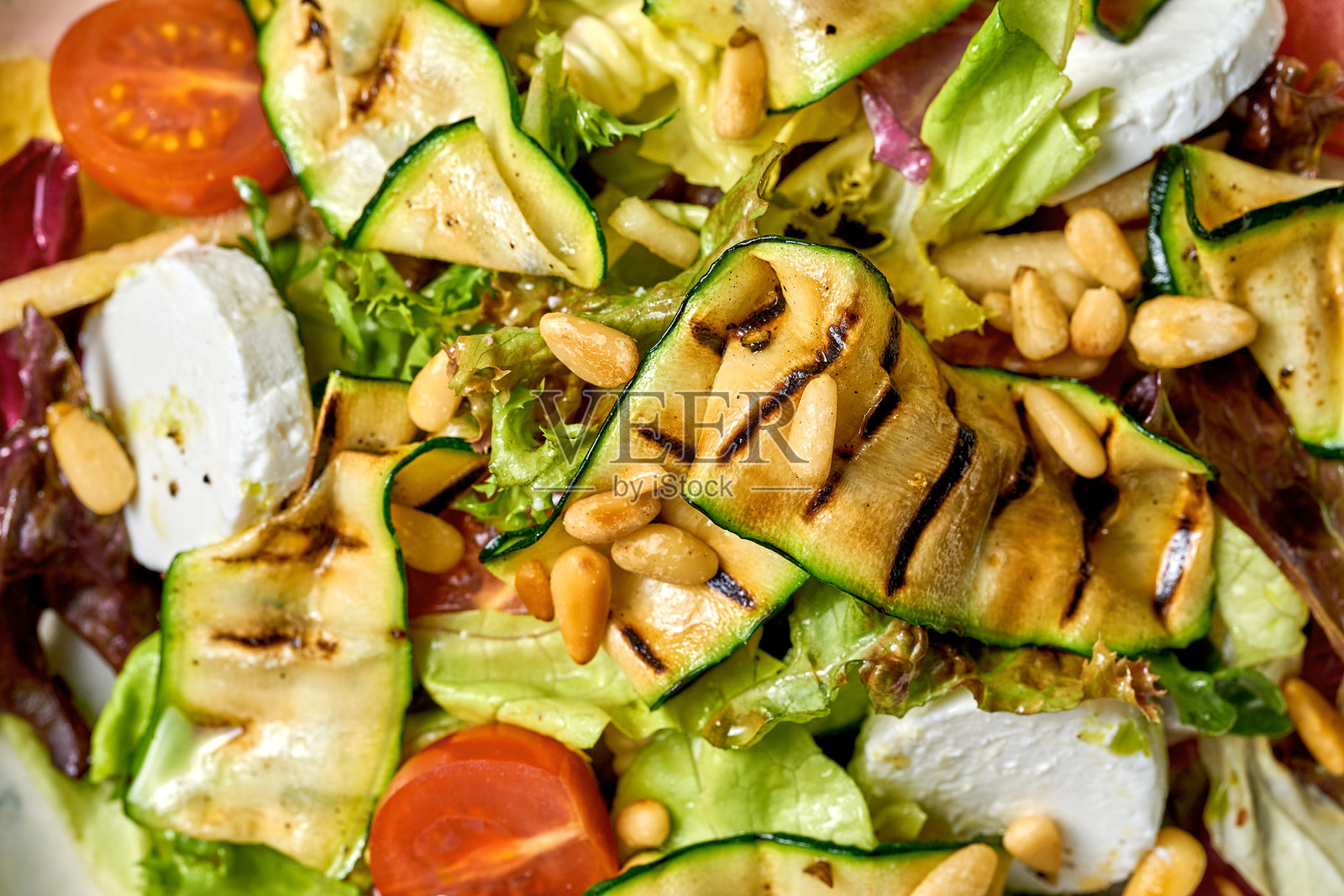 沙拉配烤西葫芦，圣女果和奶油山羊奶酪。呈现在一个白色的盘子在一个充满活力的绿色背景。照片摄影图片