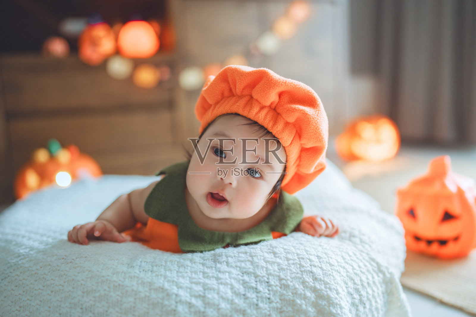 快乐可爱的亚洲新生女婴穿着万圣节杰克灯笼服装，在肚子里玩得开心，在家里庆祝万圣节照片摄影图片