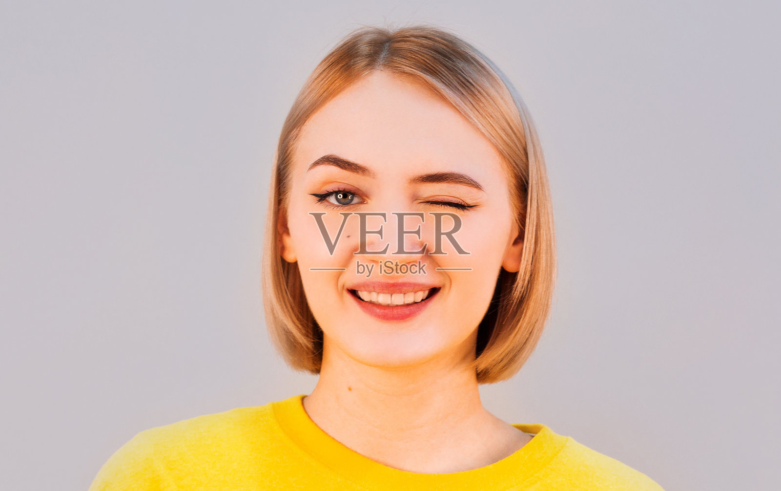 可爱的年轻女性，眉清目秀，穿着黄色的毛衣，她高兴地眨着眼睛，脸上带着幸福的表情。面部表情和人的情感概念照片摄影图片