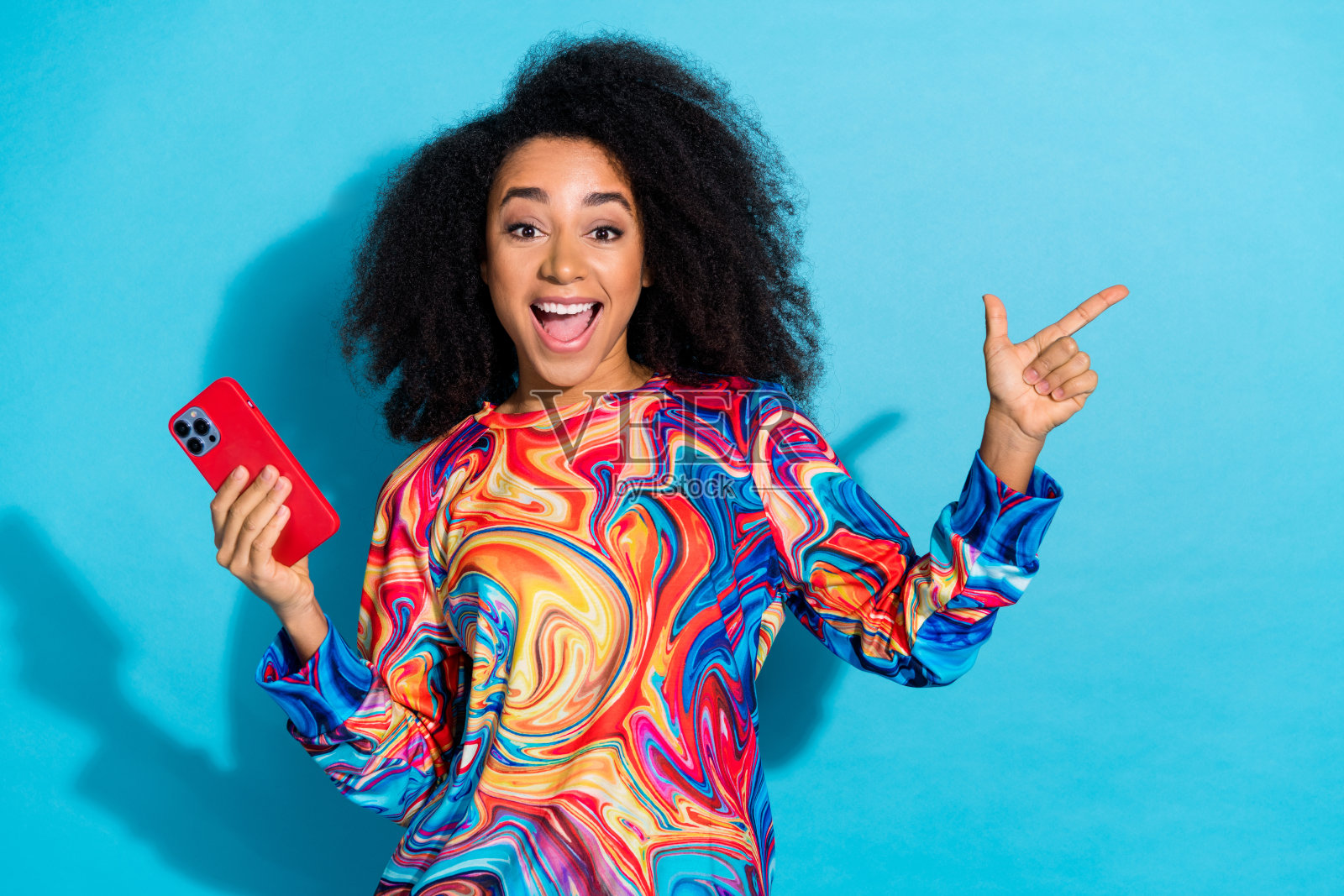 可爱的年轻女士手持设备点空的照片肖像穿着时尚的彩色服装孤立在蓝色的背景照片摄影图片