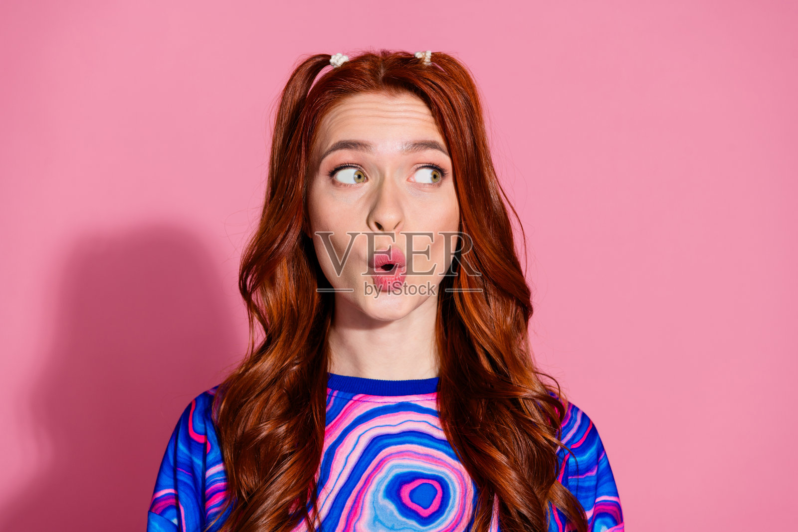 漂亮的年轻女孩的照片肖像震惊了，看起来空无一人，穿着时髦的蓝色多彩衣服，孤立在粉红色的背景上照片摄影图片