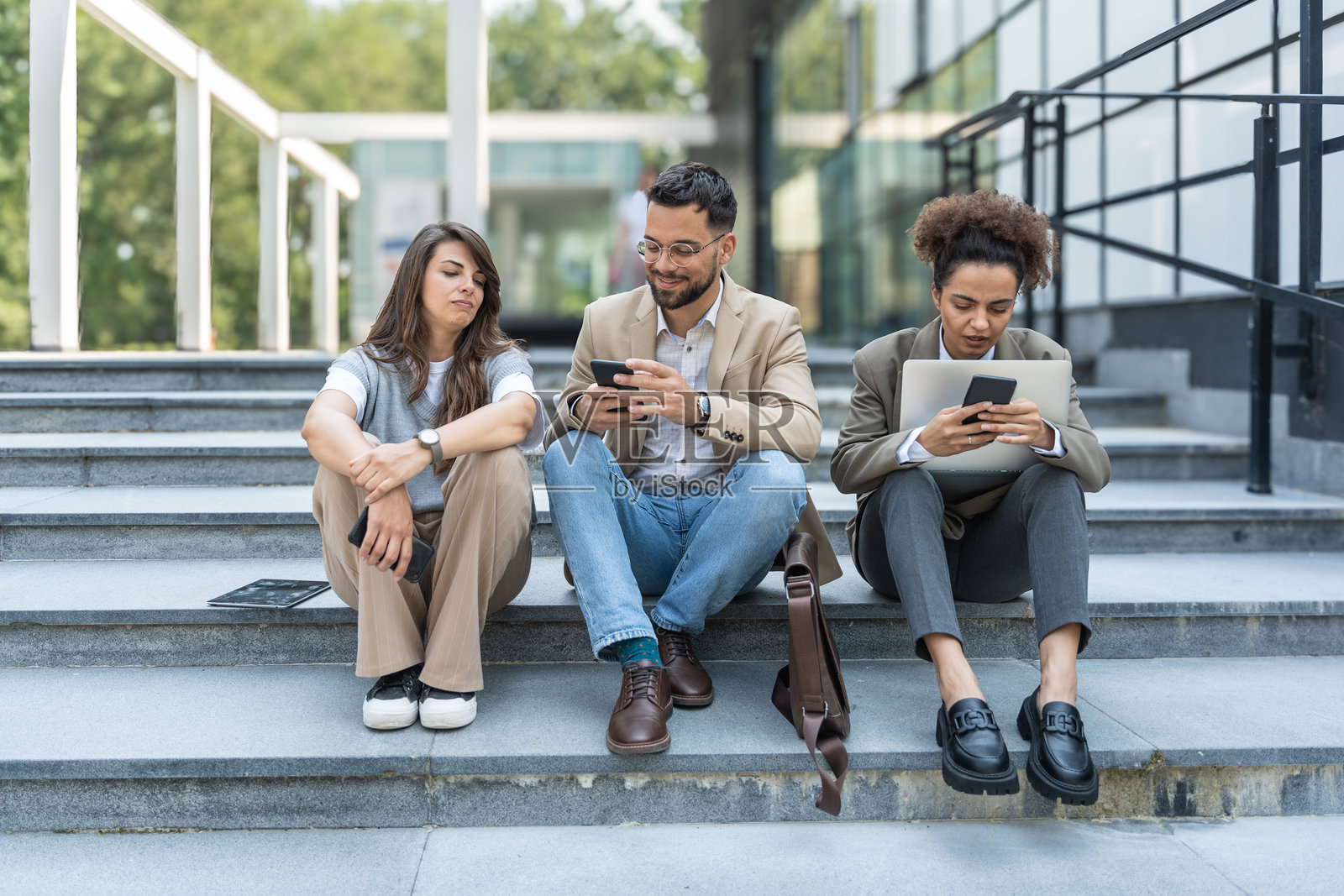 三位不同的商务人士在办公大楼外聚精会神、认真交谈，讨论计划和工作项目。商人和女商人的团队合作。照片摄影图片