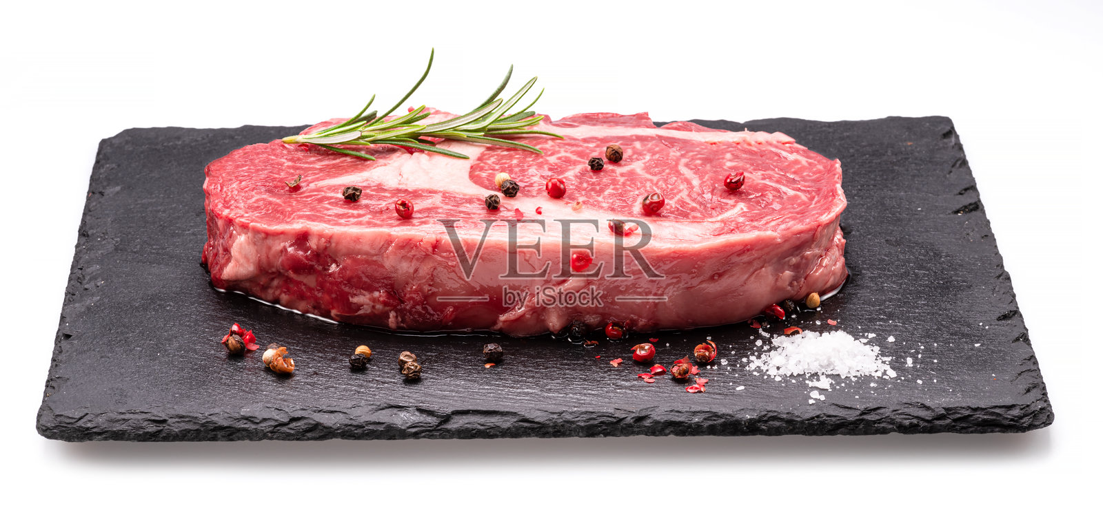 生肋眼牛排与胡椒玉米和迷迭香在石墨服务板隔离在白色背景。照片摄影图片