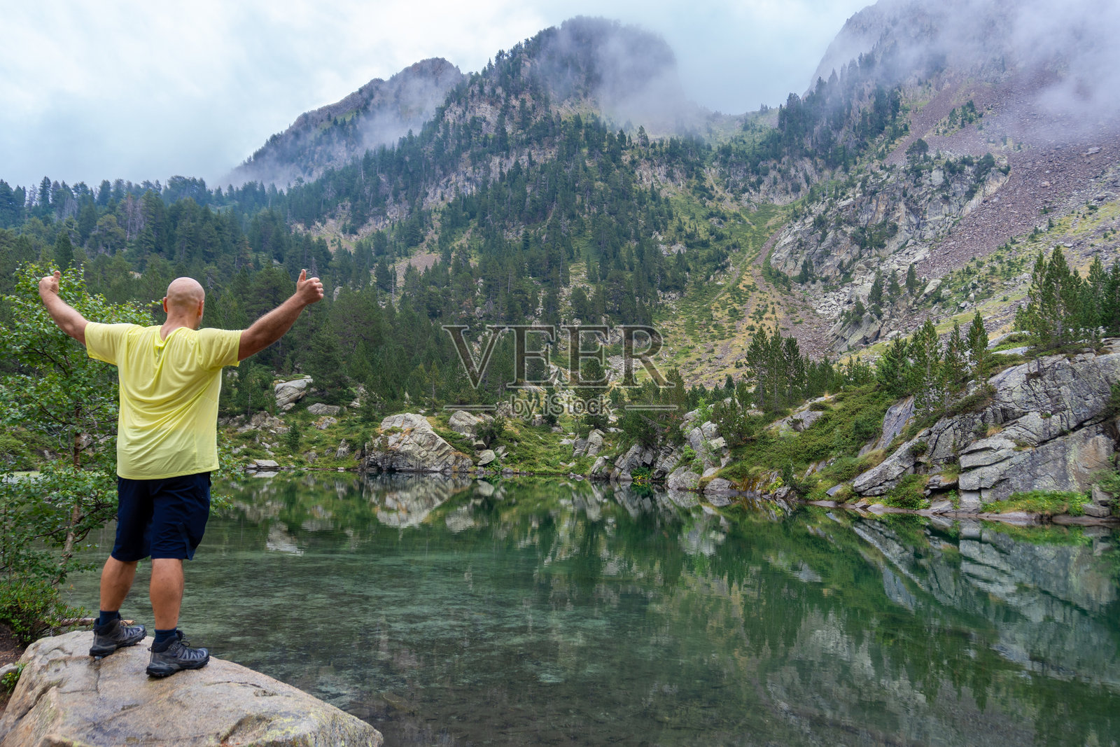 后视图，一个人在一块岩石上举起手臂，看着有湖的风景照片摄影图片