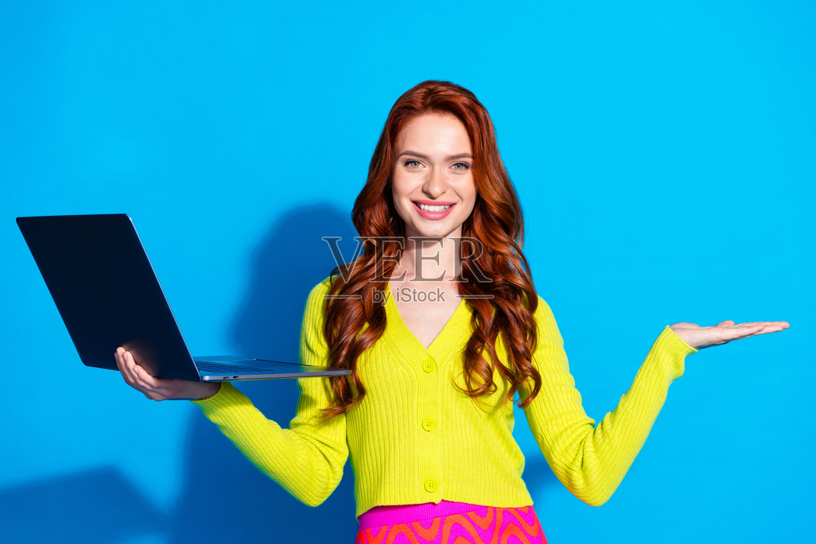 漂亮的年轻女孩的照片肖像上网本持有空白空间穿时髦的黄色服装孤立的蓝色背景照片摄影图片
