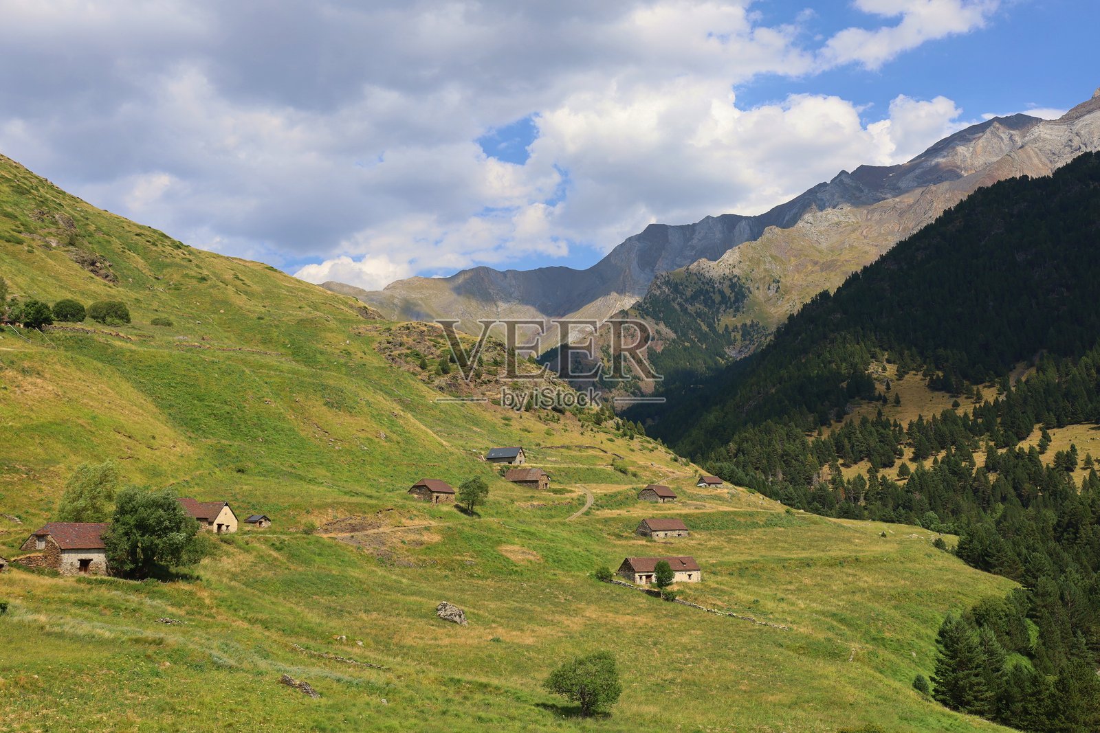 西班牙比利牛斯山脉历史悠久的维亚多斯村。绿色草地中古老的石头牧羊人小屋，波塞特山巨大的岩石墙填补了贝纳斯克旁边的图像上部照片摄影图片