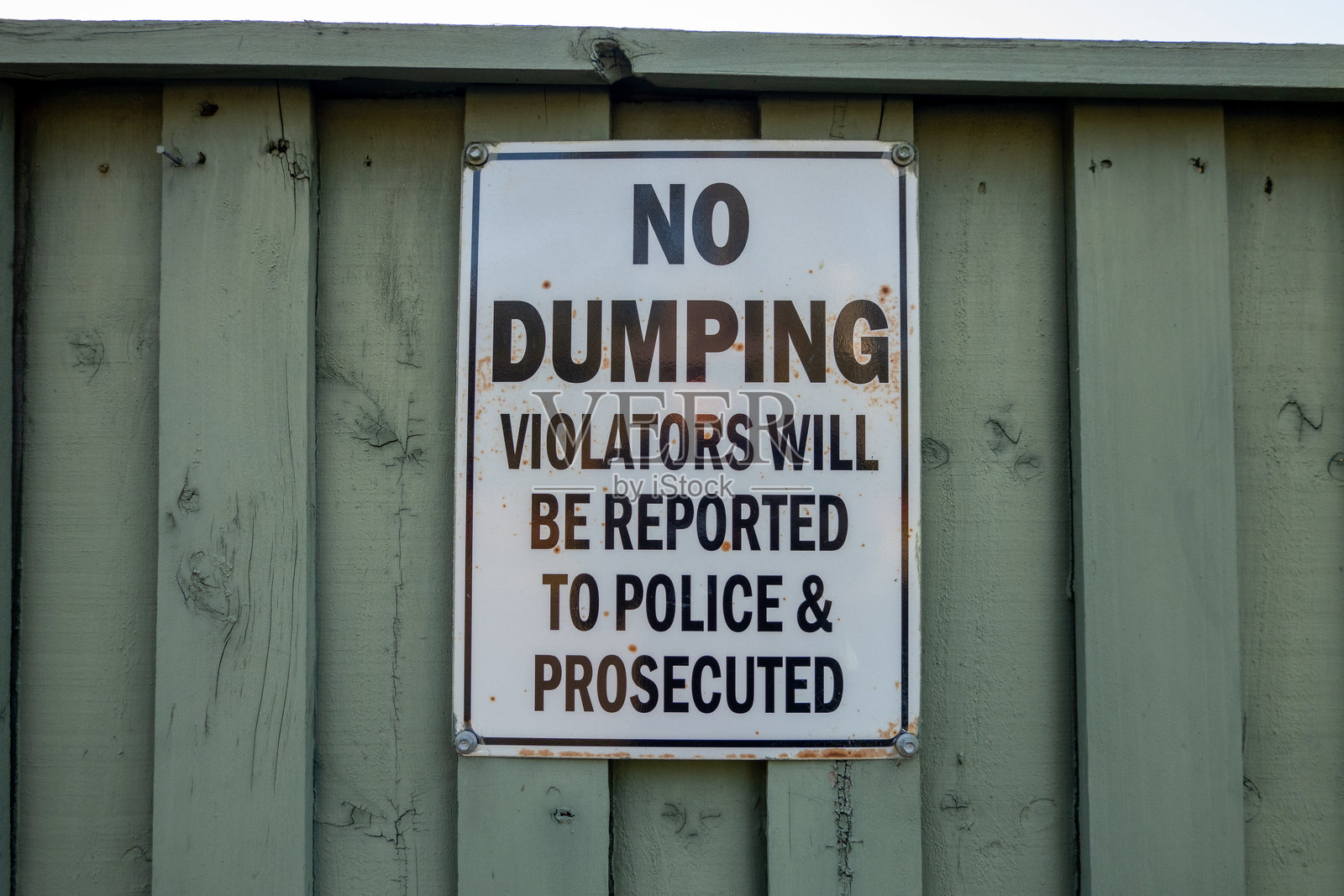 绿色木栅栏上的白色标牌上写着禁止倾倒，违规者将向警方报案并受到起诉照片摄影图片