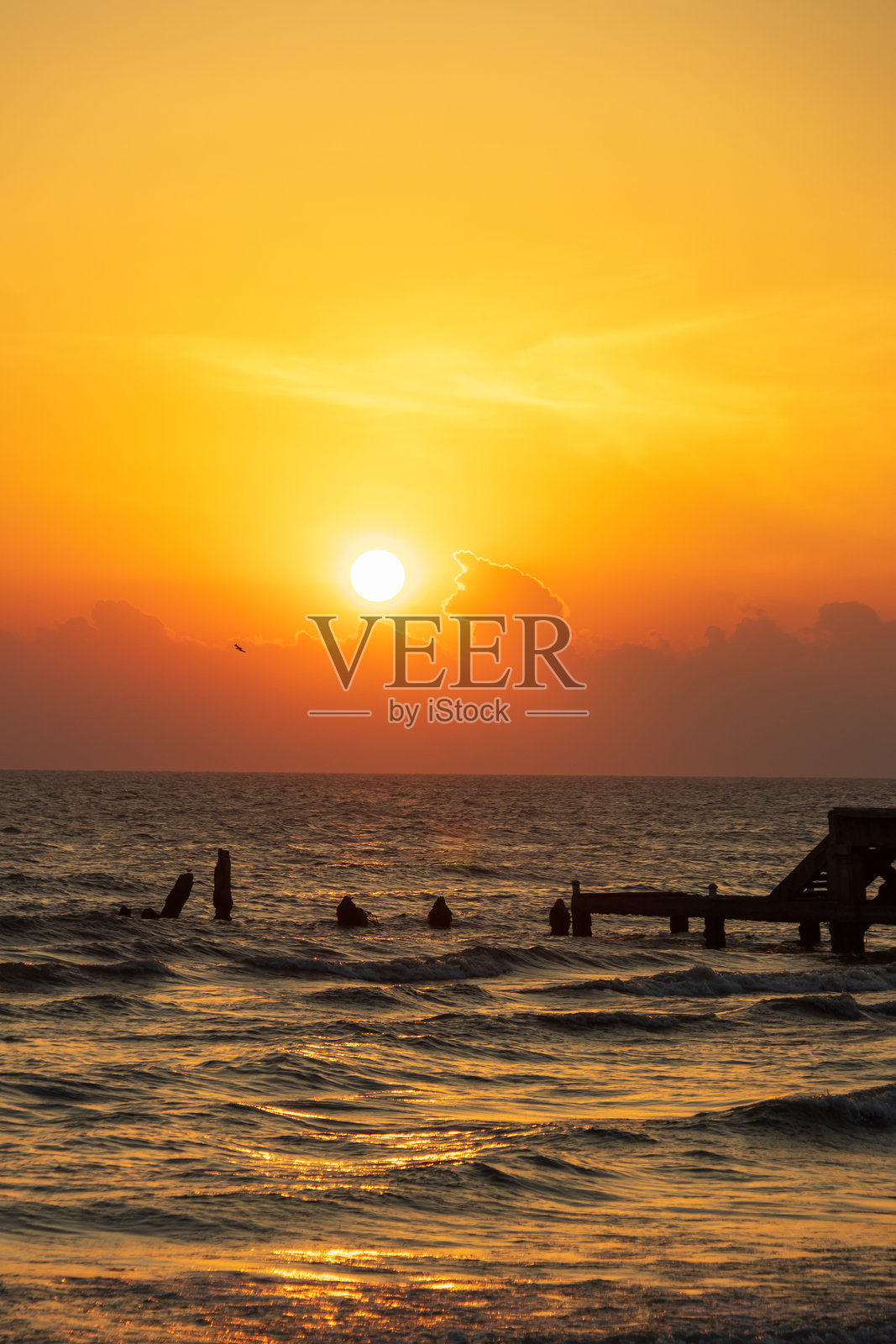 一个宁静的日落在海洋上，投下温暖的色调横跨水面与轮廓的码头和遥远的海浪。照片摄影图片