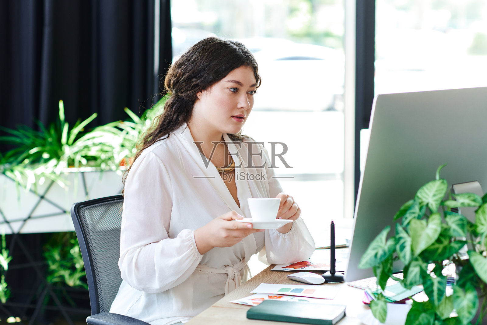 一位穿着时尚服装的大码女士在现代的工作空间里品味着咖啡照片摄影图片