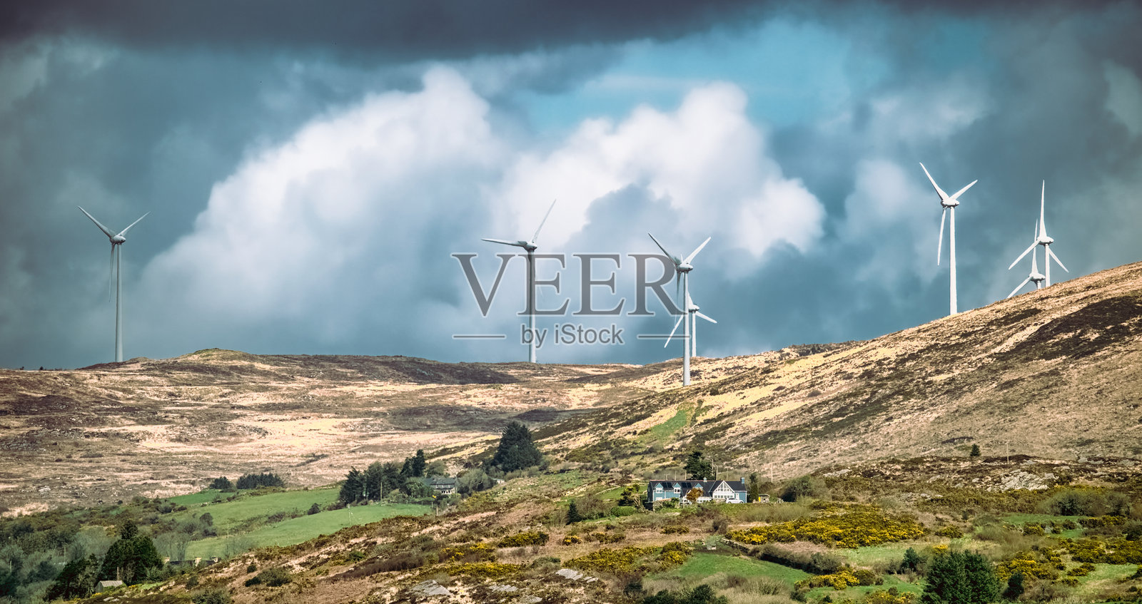 很少有风力涡轮机高高矗立在山坡上，在多云的天空下捕捉风能。照片摄影图片