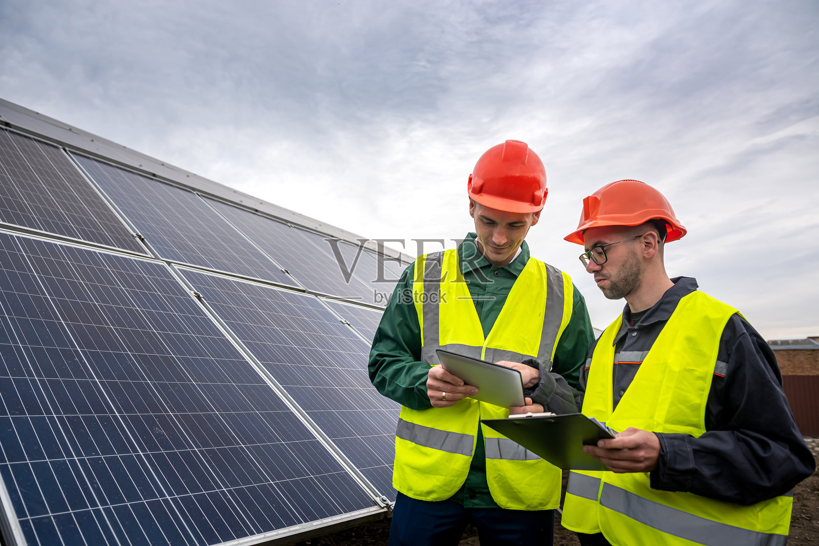 两个身强力壮、技术娴熟的男人，戴着头盔，穿着背心，站在太阳能板上聊天。照片摄影图片