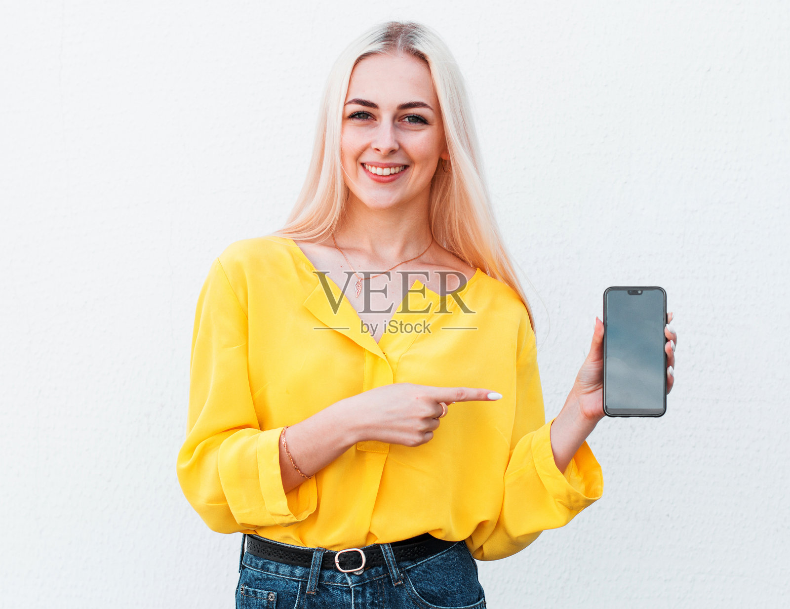 一名女子微笑着指着白色背景上的智能手机。照片摄影图片