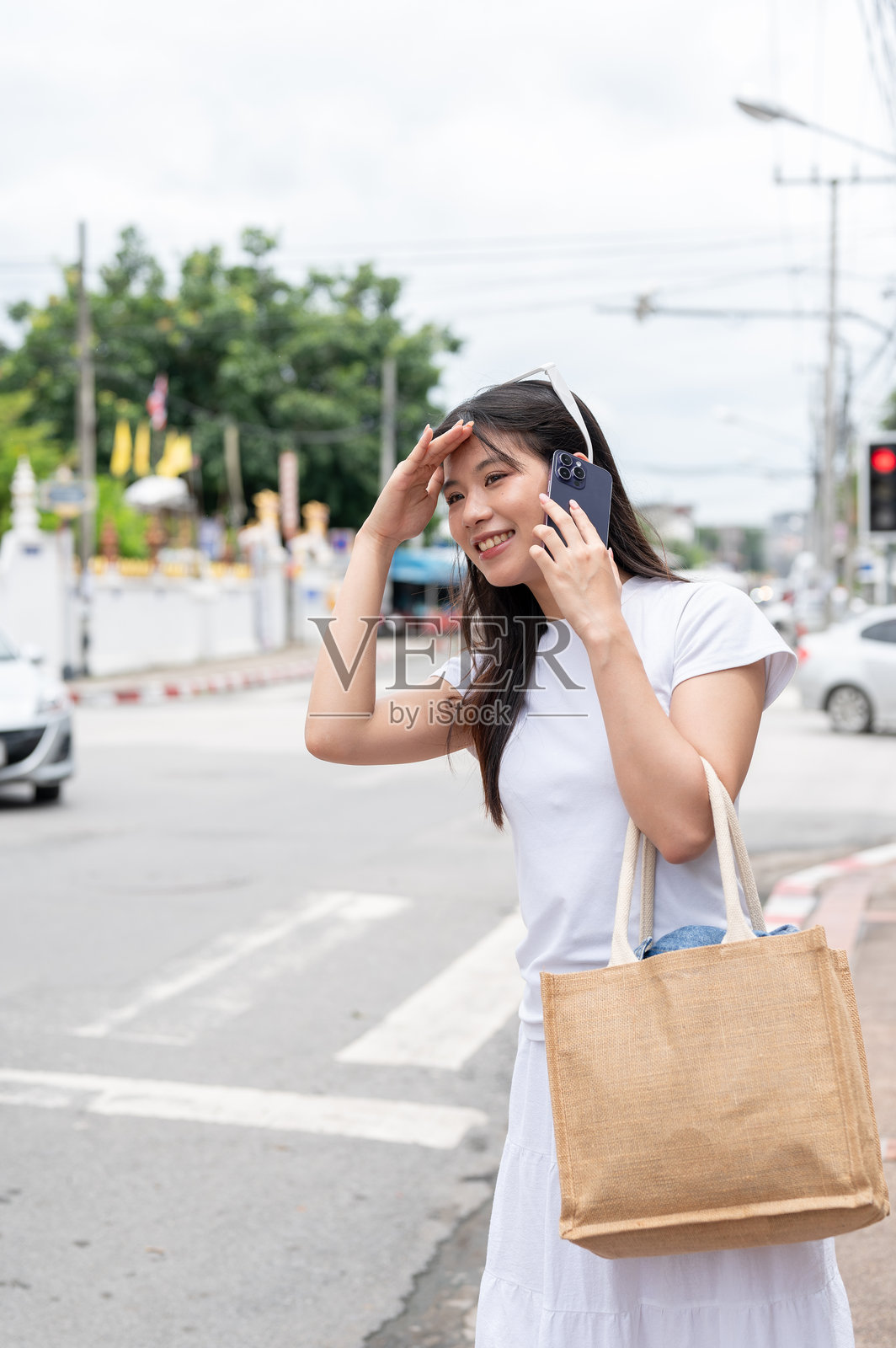 一位乐观的亚洲妇女在城市的街道边打电话边找出租车。照片摄影图片