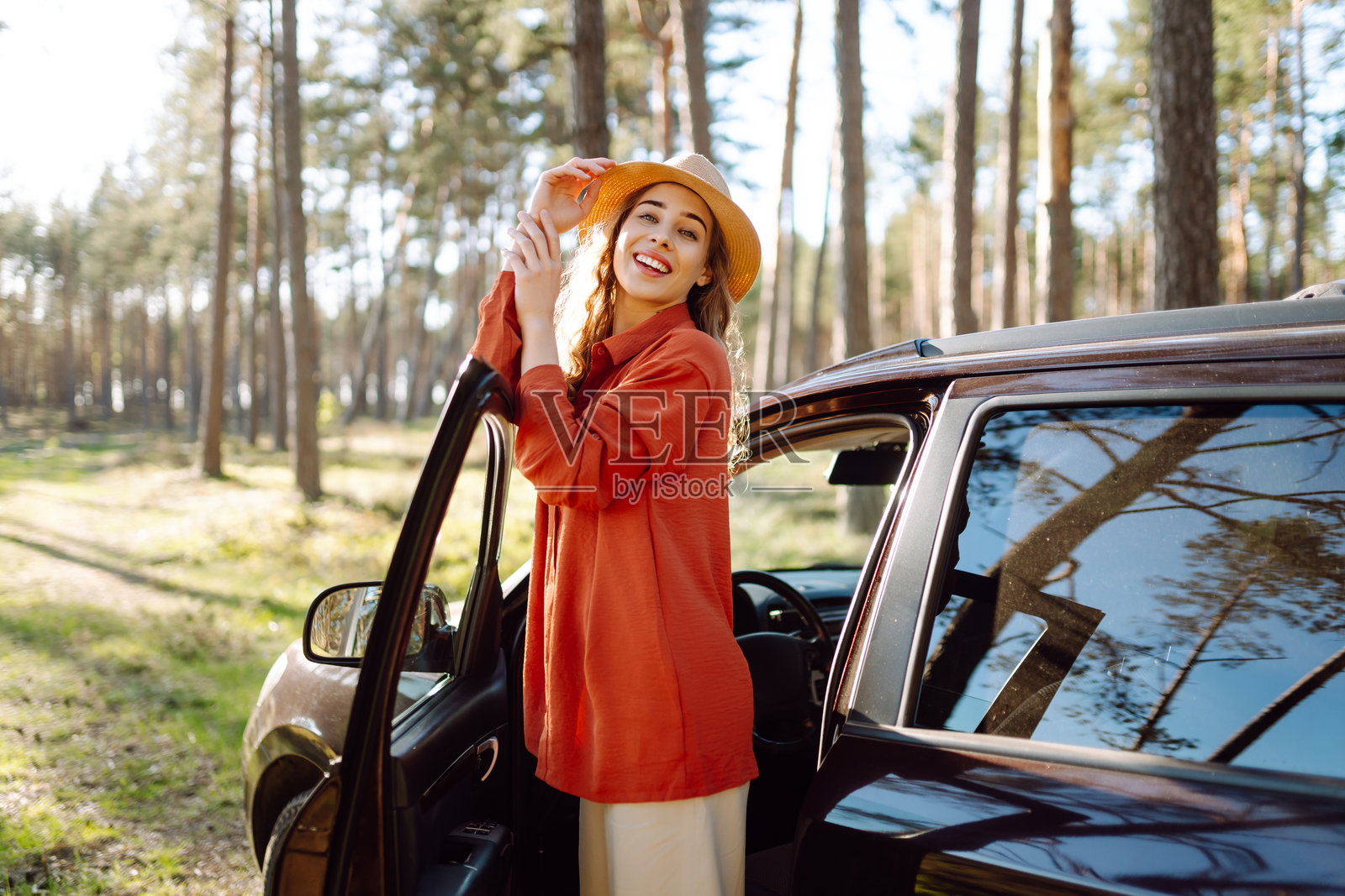 下午，在宁静的森林里，年轻女子坐在车里享受着阳光明媚的一天。照片摄影图片