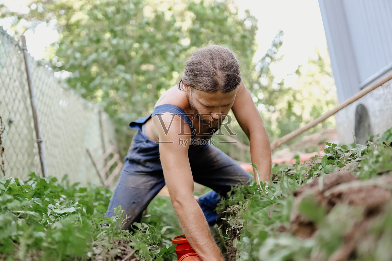 一名男水管工在一所房子的院子里安装下水管道。照片摄影图片