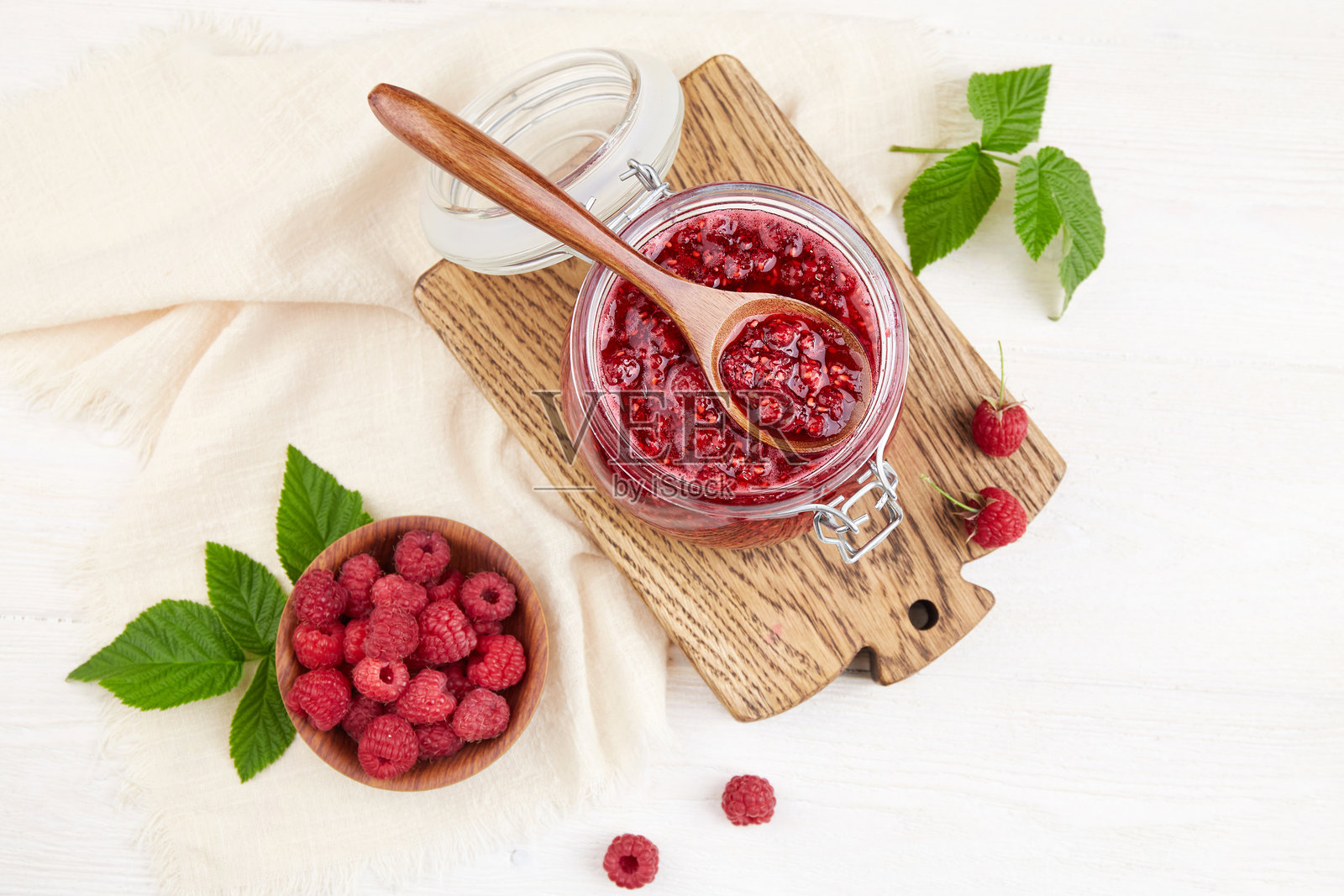 一罐覆盆子果酱和一碗新鲜的浆果放在一张白色的木桌上。照片摄影图片