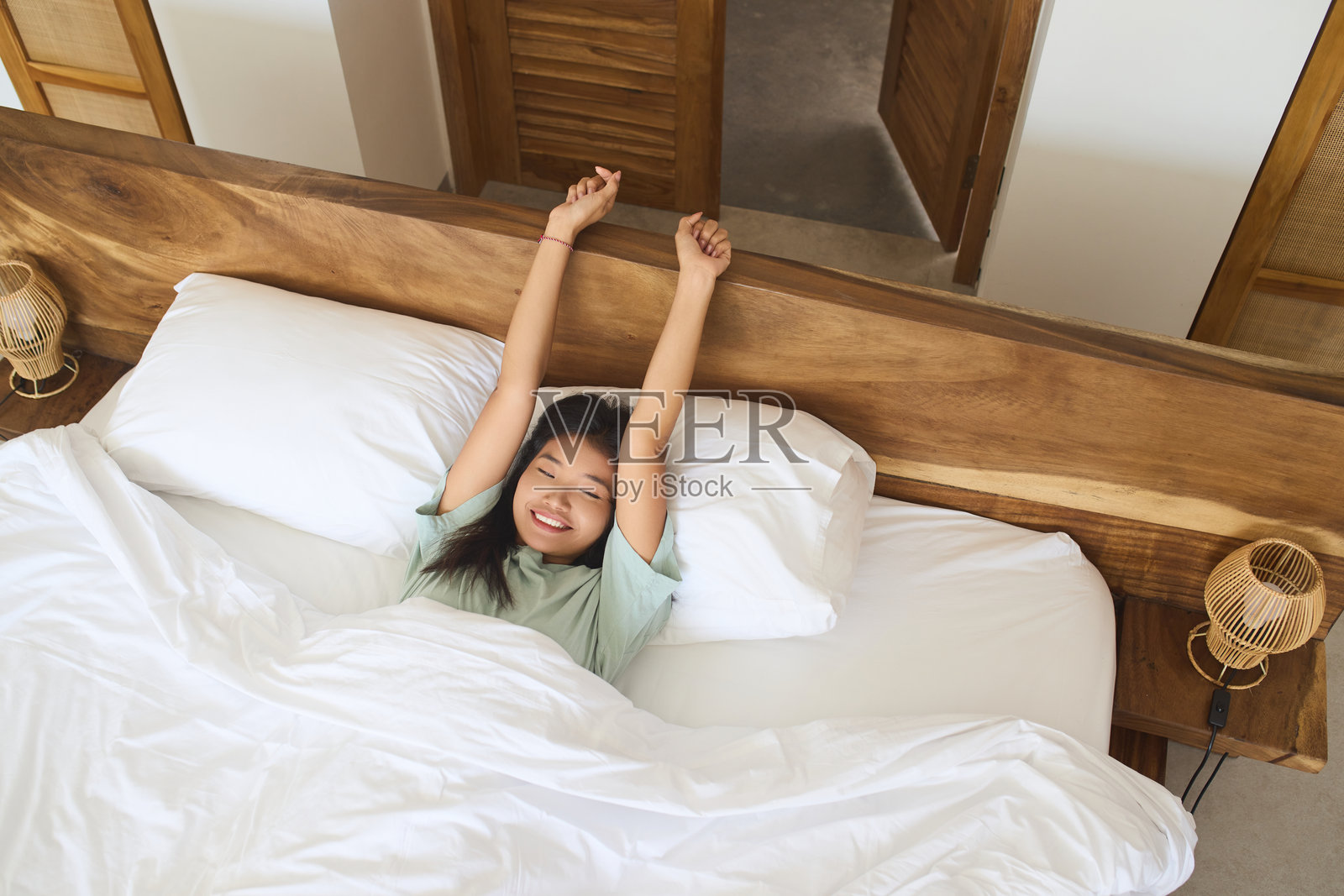 早晨醒来后，女人微笑着躺在床上伸展身体照片摄影图片