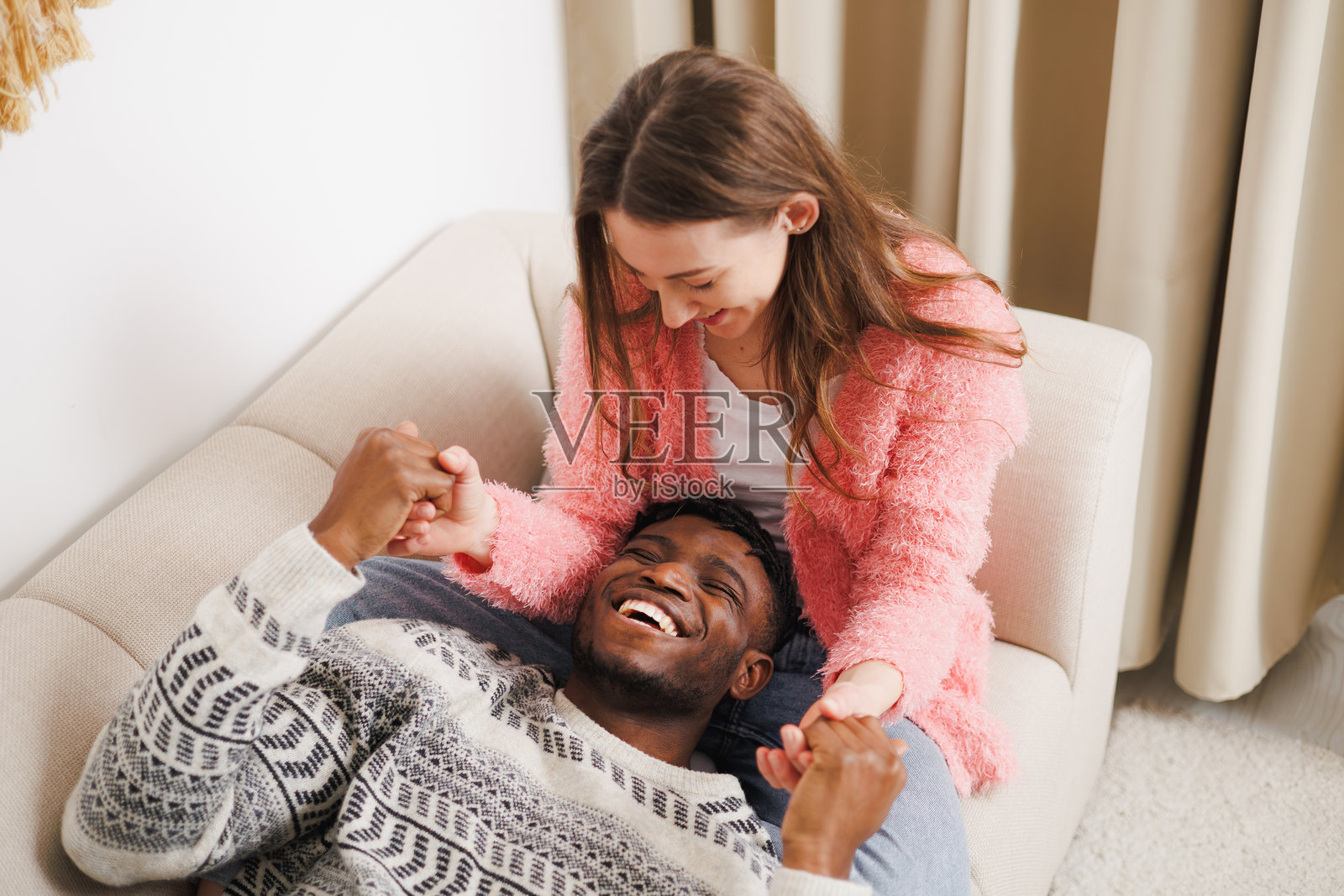 在家里的沙发上，微笑的女人牵着非裔美国男友的手照片摄影图片