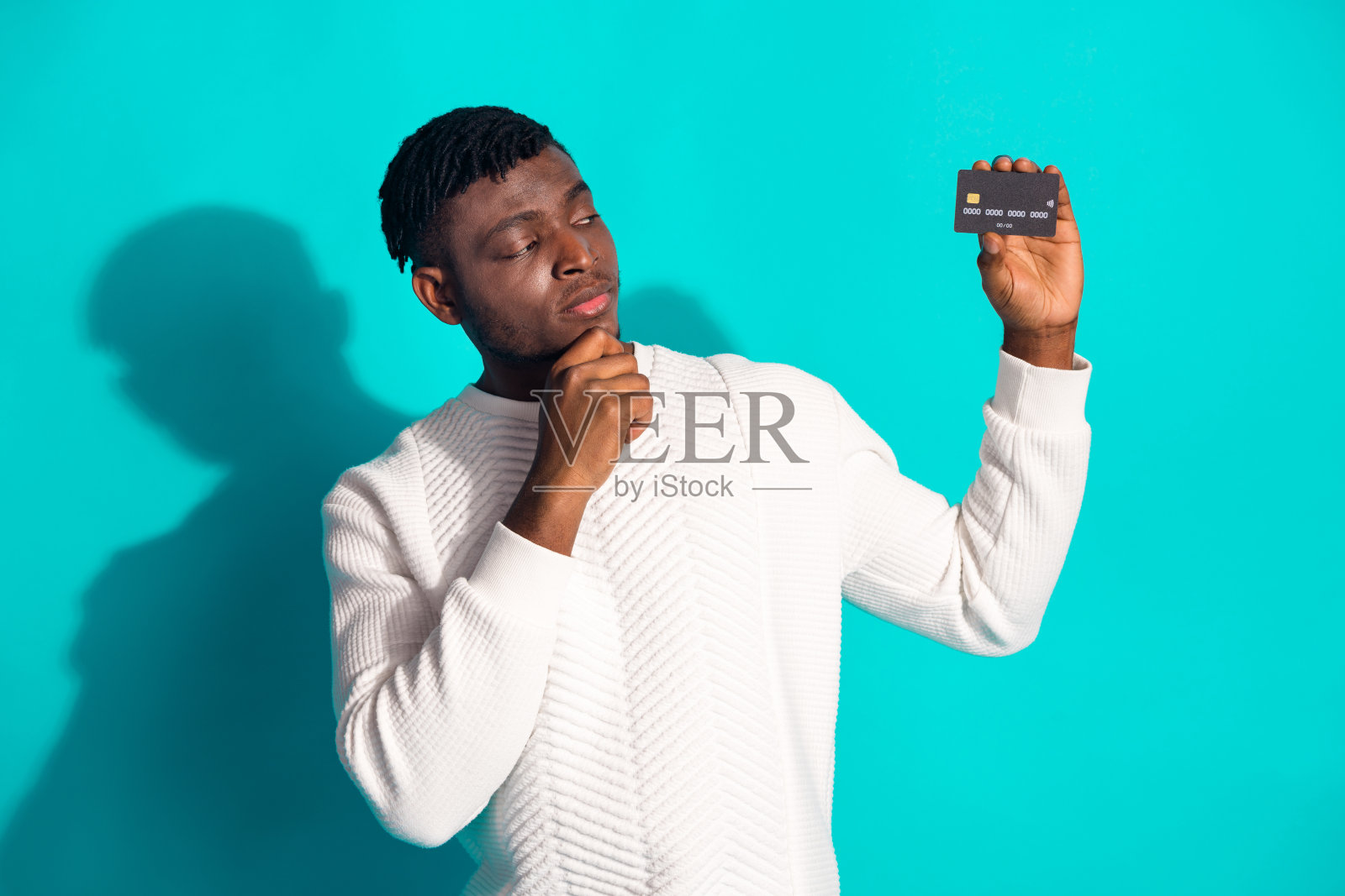 照片肖像漂亮的年轻男性看起来怀疑的信用卡穿着时髦的白色衣服孤立的海蓝宝石色背景照片摄影图片