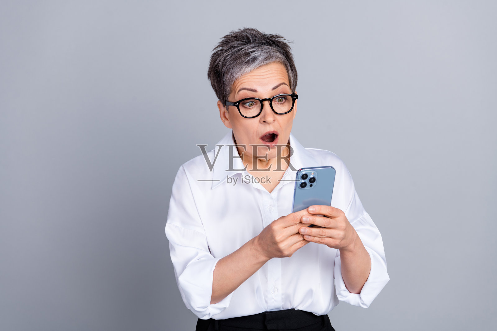 迷人的退休妇女的照片肖像惊讶地拿着小玩意，穿着时尚的正装，孤立在灰色背景上照片摄影图片