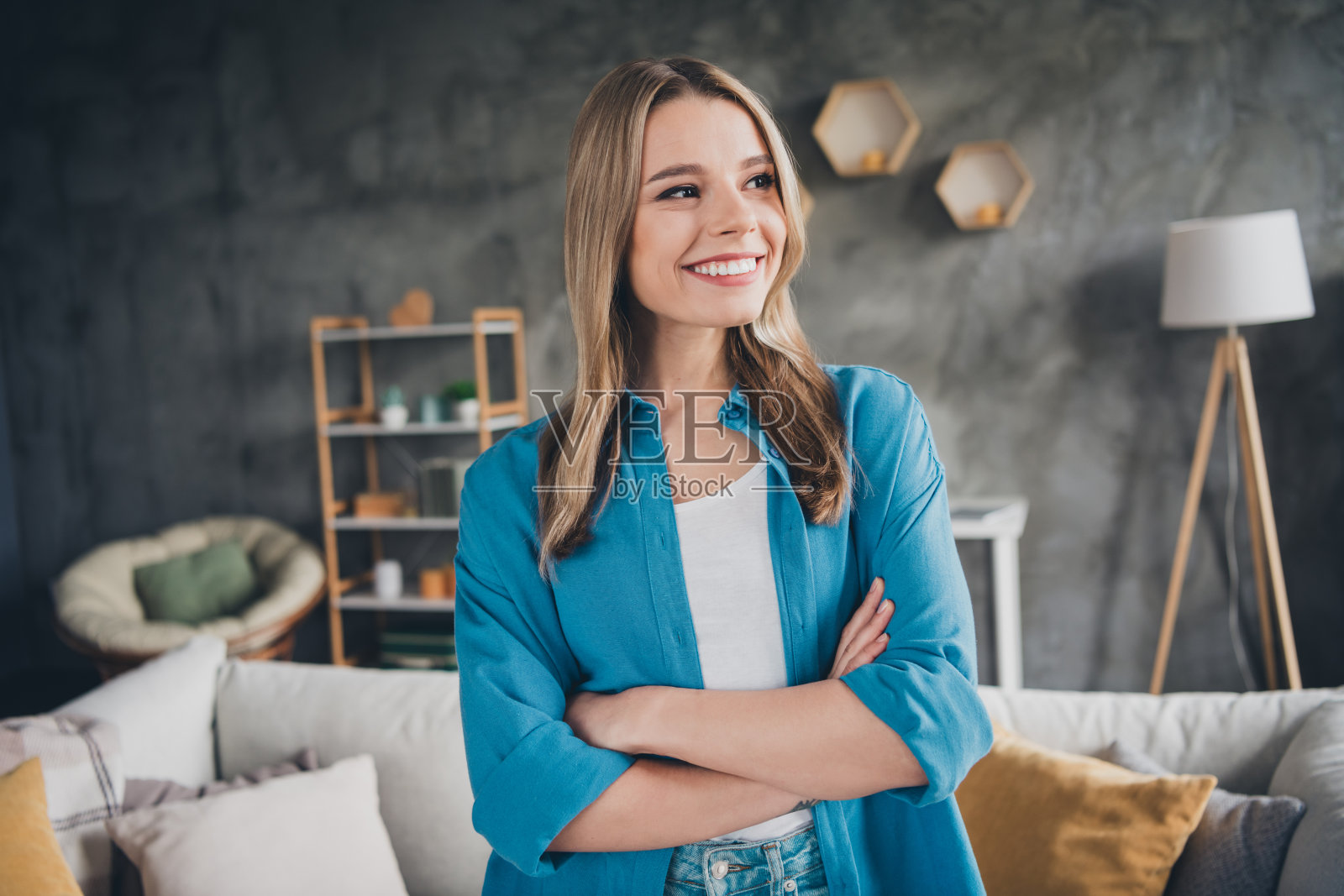 开朗的金发年轻女孩的肖像，穿着蓝色衬衫，沉思，双臂交叉，对现代设计工作室家具充满信心照片摄影图片