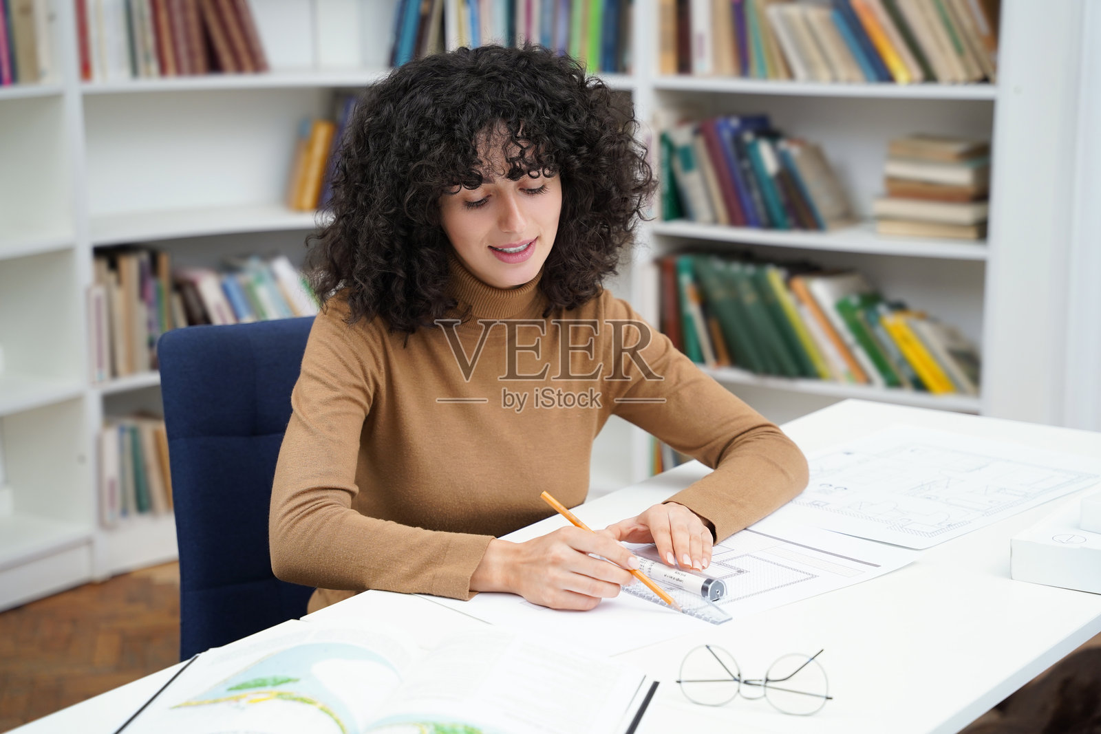 可爱的年轻卷发女人坐在图书馆的桌子旁照片摄影图片