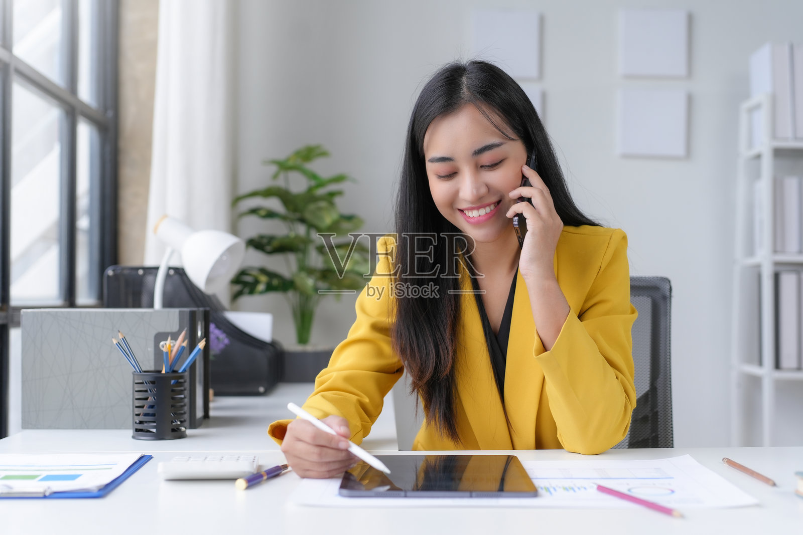 亚洲女商人在办公室里打电话，用平板电脑做笔记照片摄影图片