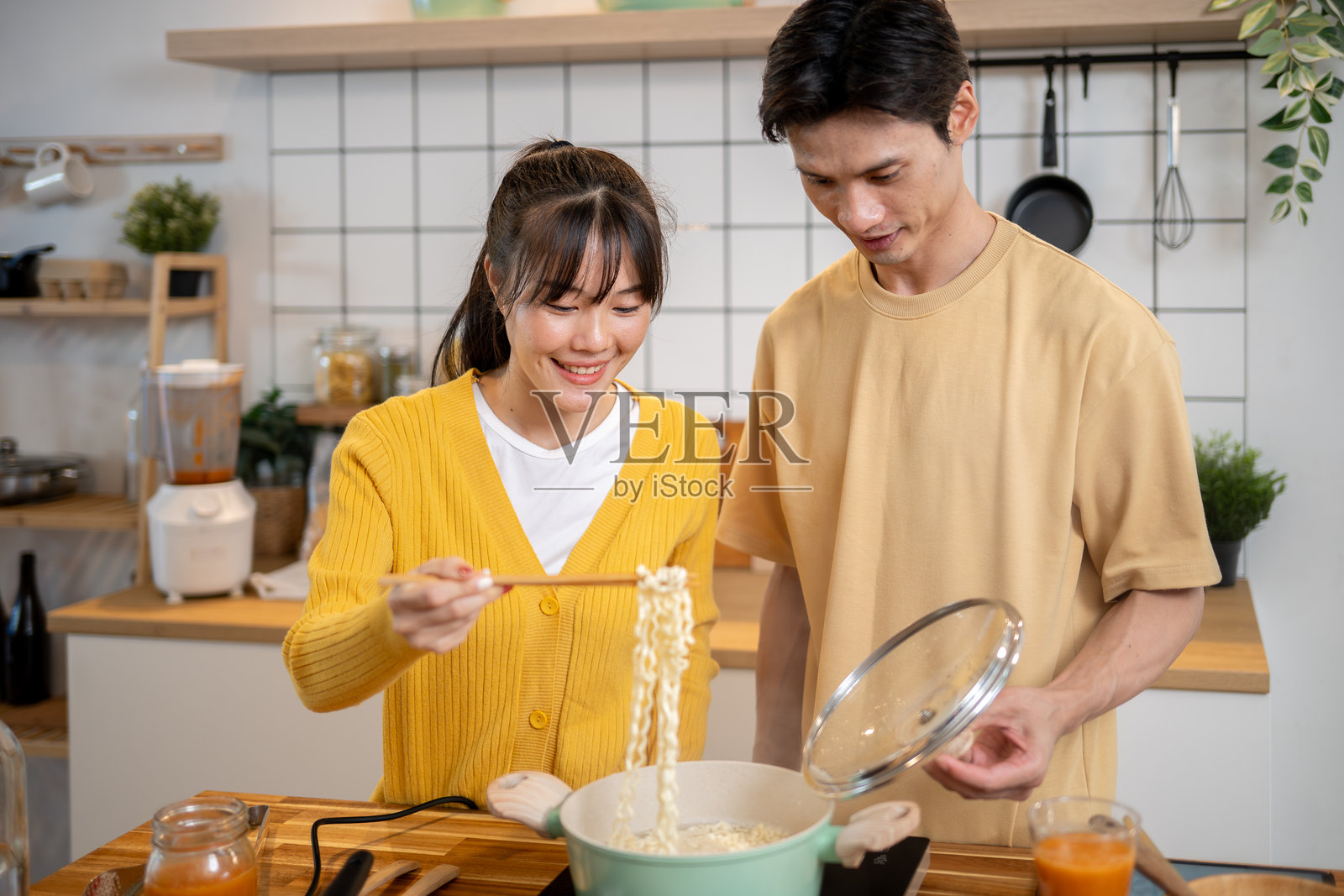 一对可爱的年轻亚洲夫妇正在厨房里享受着一起做面条的乐趣。照片摄影图片