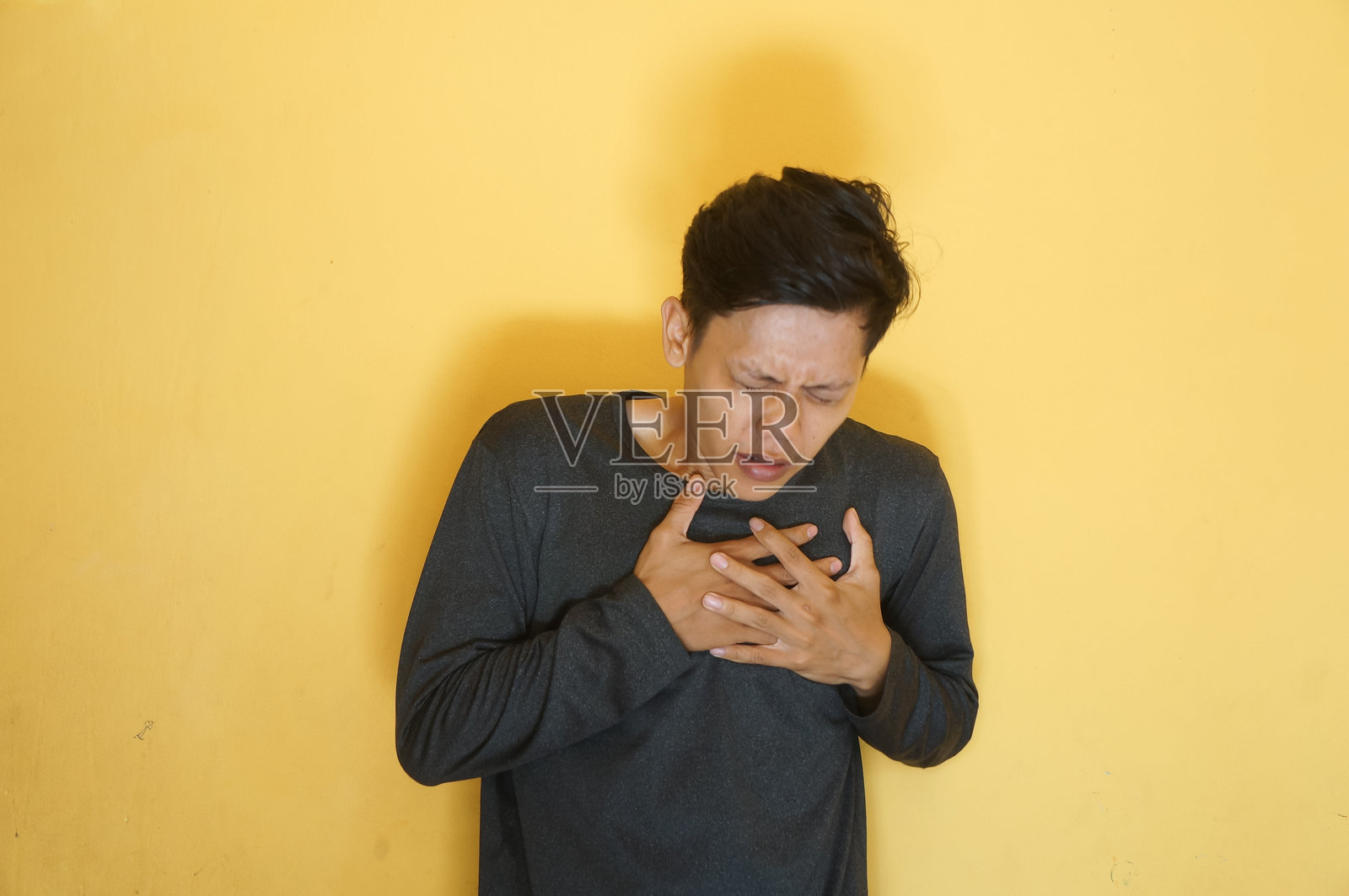 穿着黑色t恤，胸痛表情的亚洲年轻人照片摄影图片