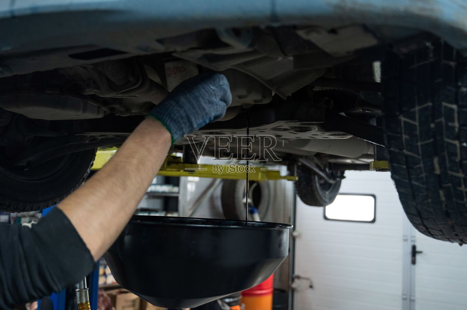 给汽车发动机换油的过程。在电梯里把车里的旧机油抽干。照片摄影图片