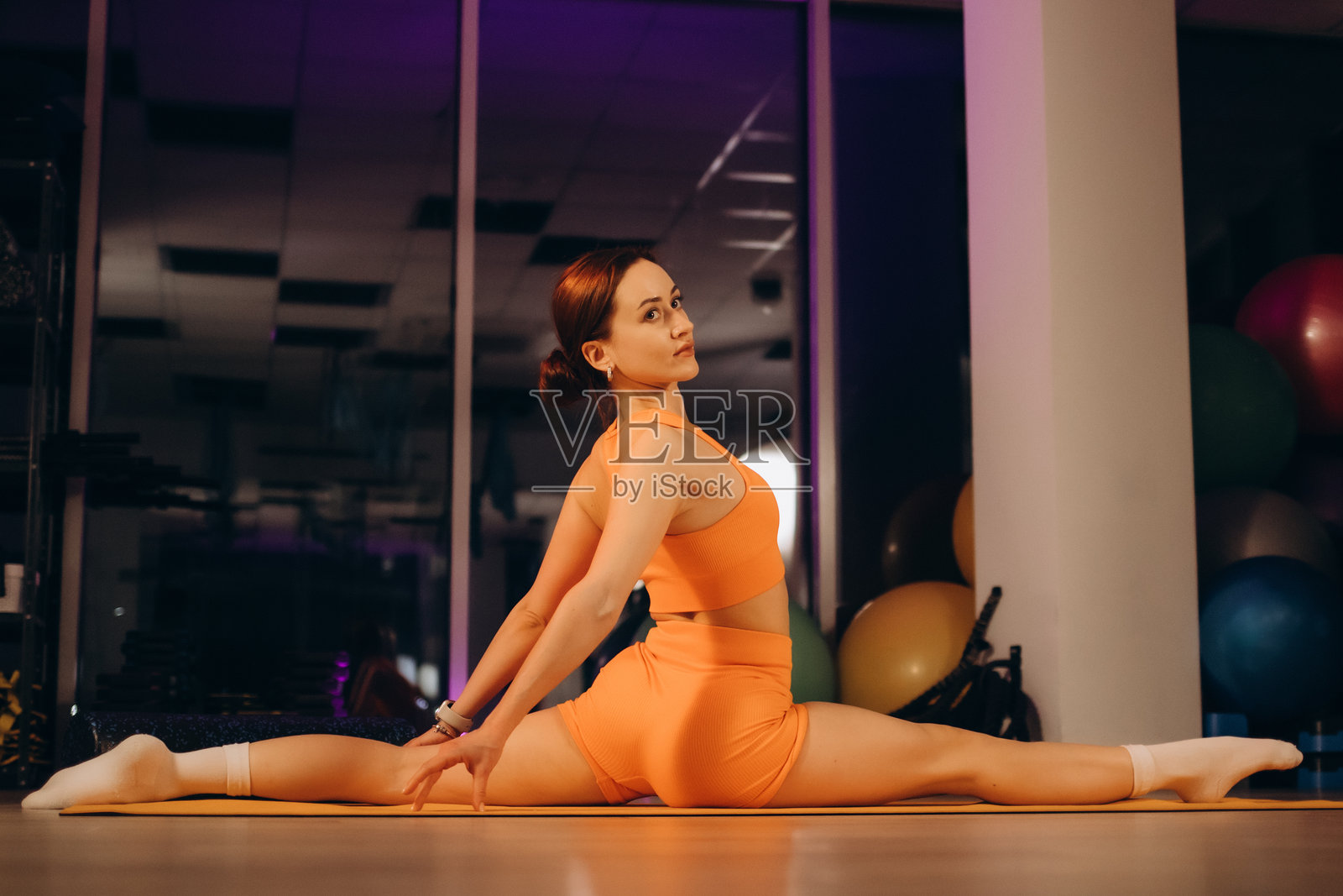 运动健身活跃的年轻文身女子在运动服伸展坐腿分开在地板上健身工作室，女性健康的女孩做运动体操锻炼运动健身训练的理念。照片摄影图片
