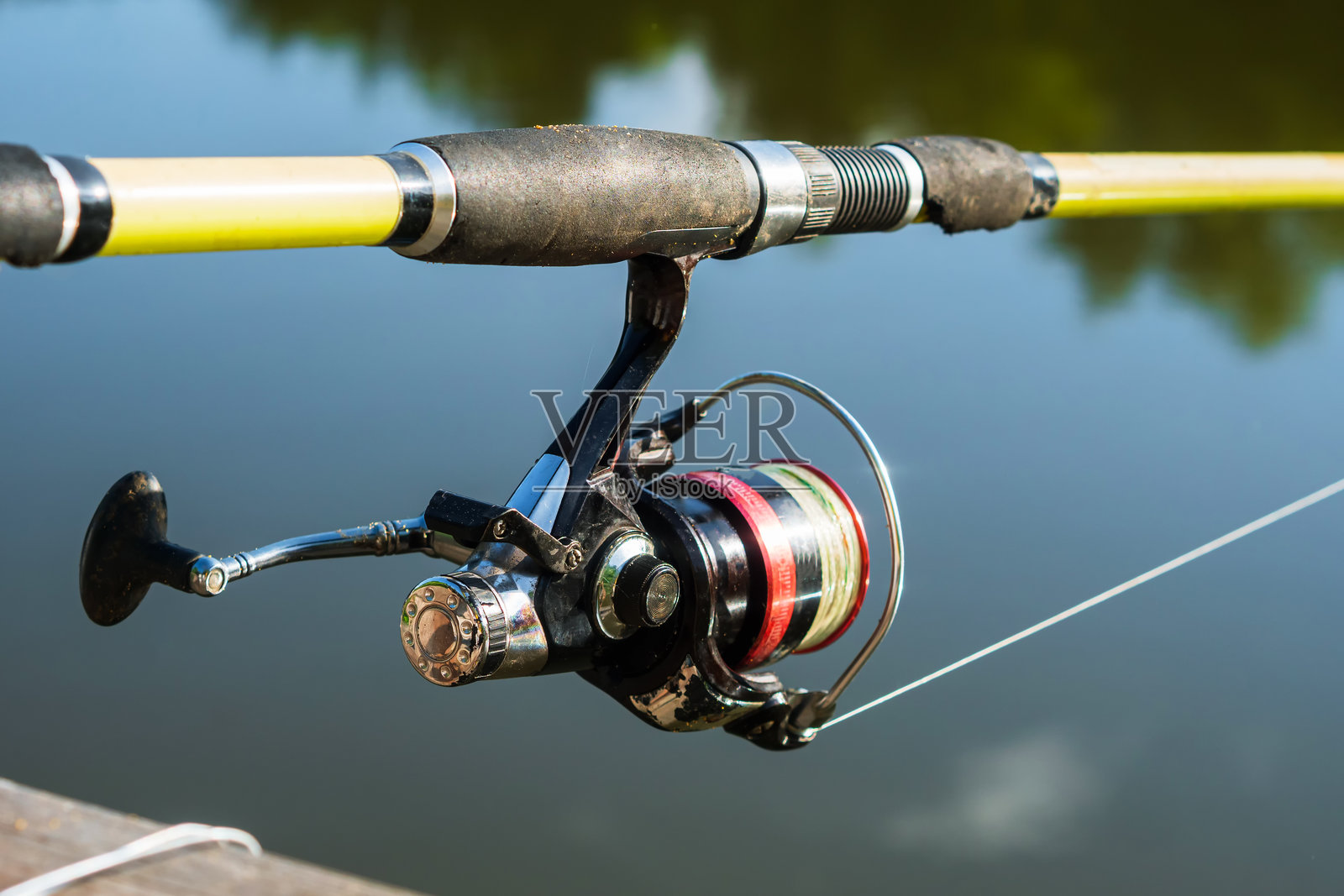 一根又旧又旧的纺线杆，上面有一个红色的卷轴，映衬着池塘里蓝色的水照片摄影图片