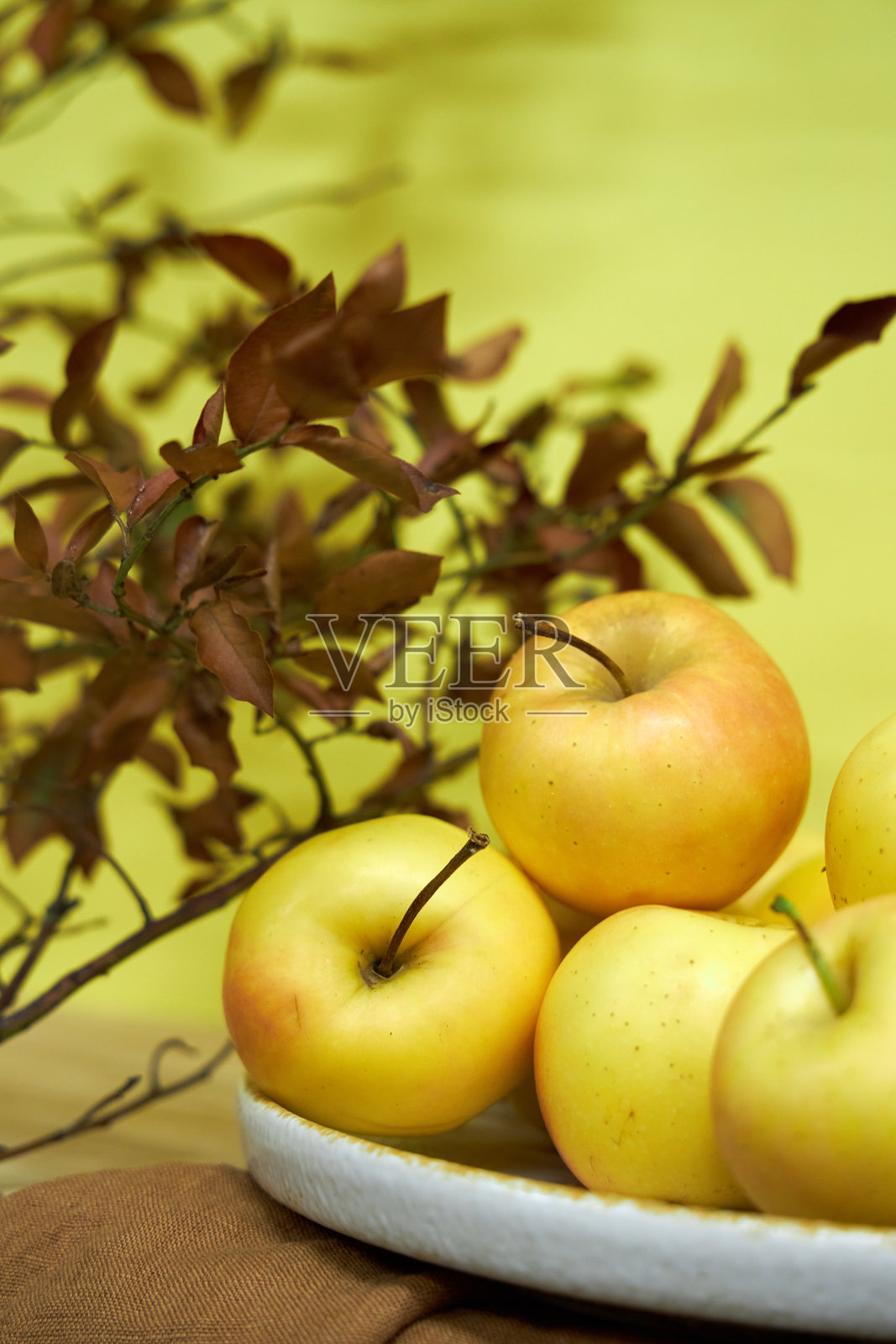 盘子上有黄色背景的黄色苹果和棕色树枝。现代极简静物，黄色照片摄影图片