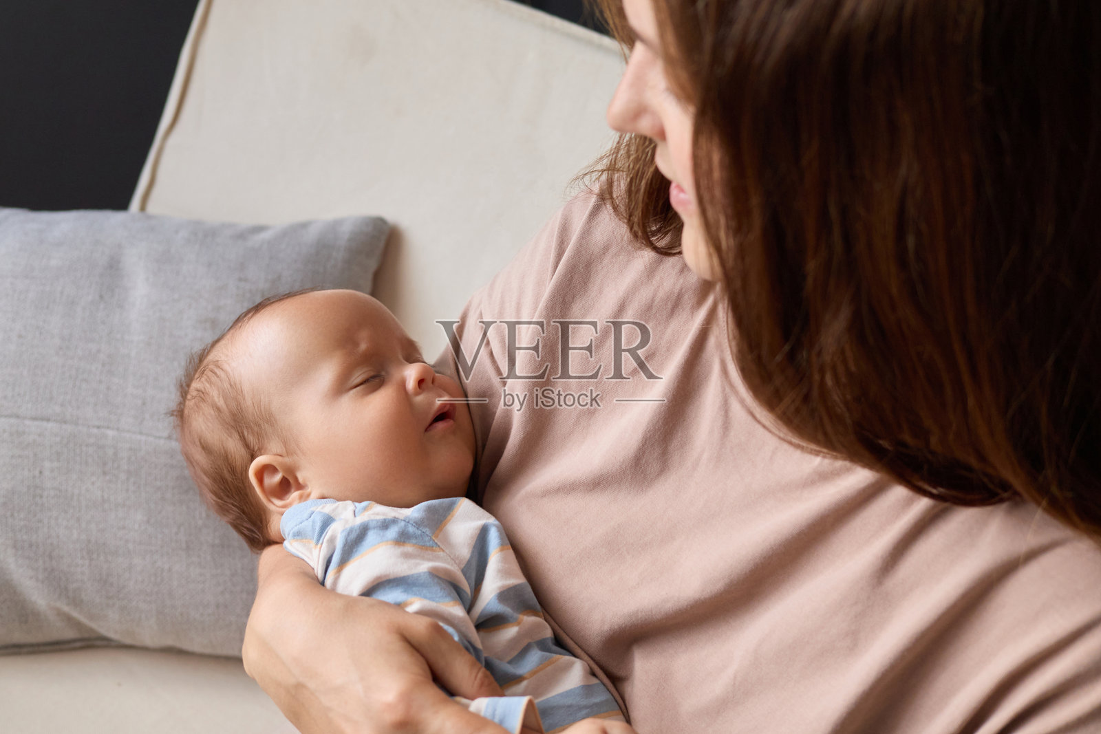穿着条纹衣服的小婴儿特写，母亲抱着熟睡的儿子或女儿坐在客厅的沙发上，摇晃着她刚出生的婴儿照片摄影图片