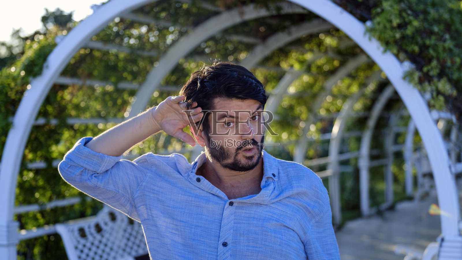 夏日里，在一个阳光明媚、绿树成荫的公园里，一位身穿衬衫、黑发的中年商人看着镜头，他的手势和面部表情显示出他被炎热难耐了照片摄影图片