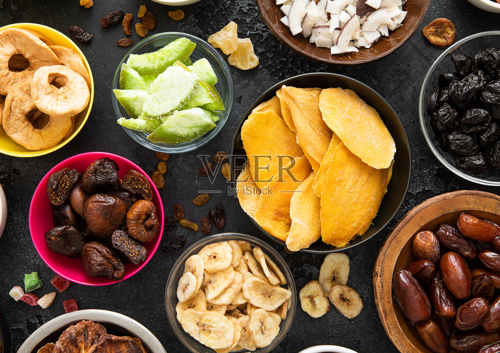 什锦有机健康干甜浆果和水果小吃在各种碗盘黑色背景。前视图。照片摄影图片