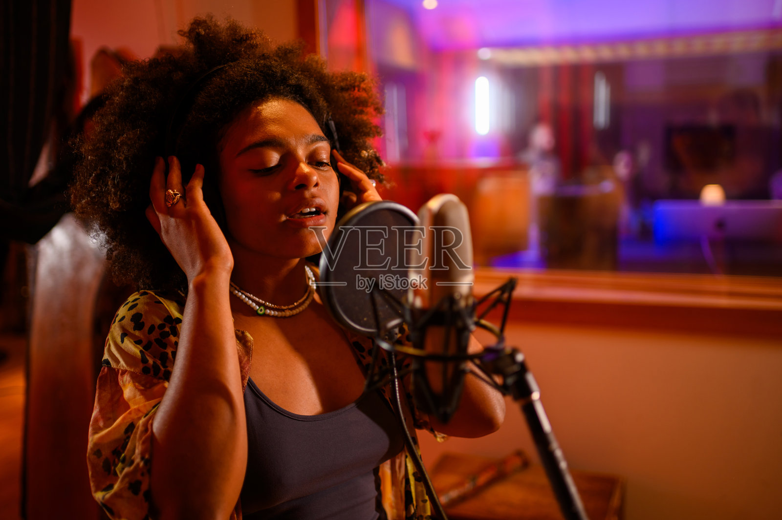 在音乐工作室，不同的歌手带着耳机对着麦克风唱歌照片摄影图片