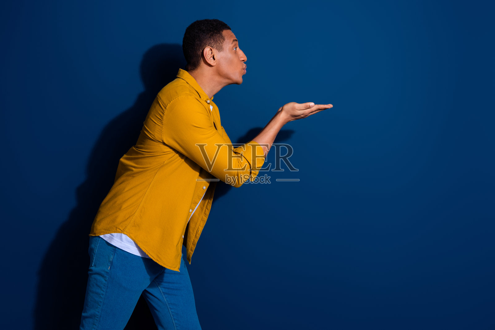 漂亮的年轻人的侧面肖像送空吻空空间穿着黄色衬衫孤立在深蓝色的背景照片摄影图片