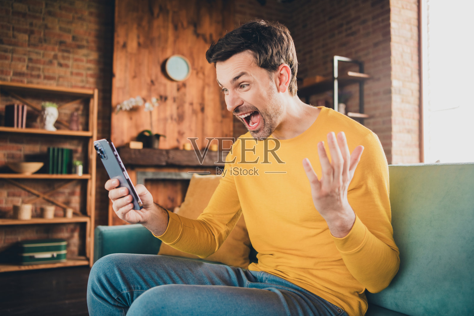 漂亮年轻人的照片肖像激动地拿着设备新闻坐在沙发上穿着黄色的衣服现代室内平坦的室内照片摄影图片